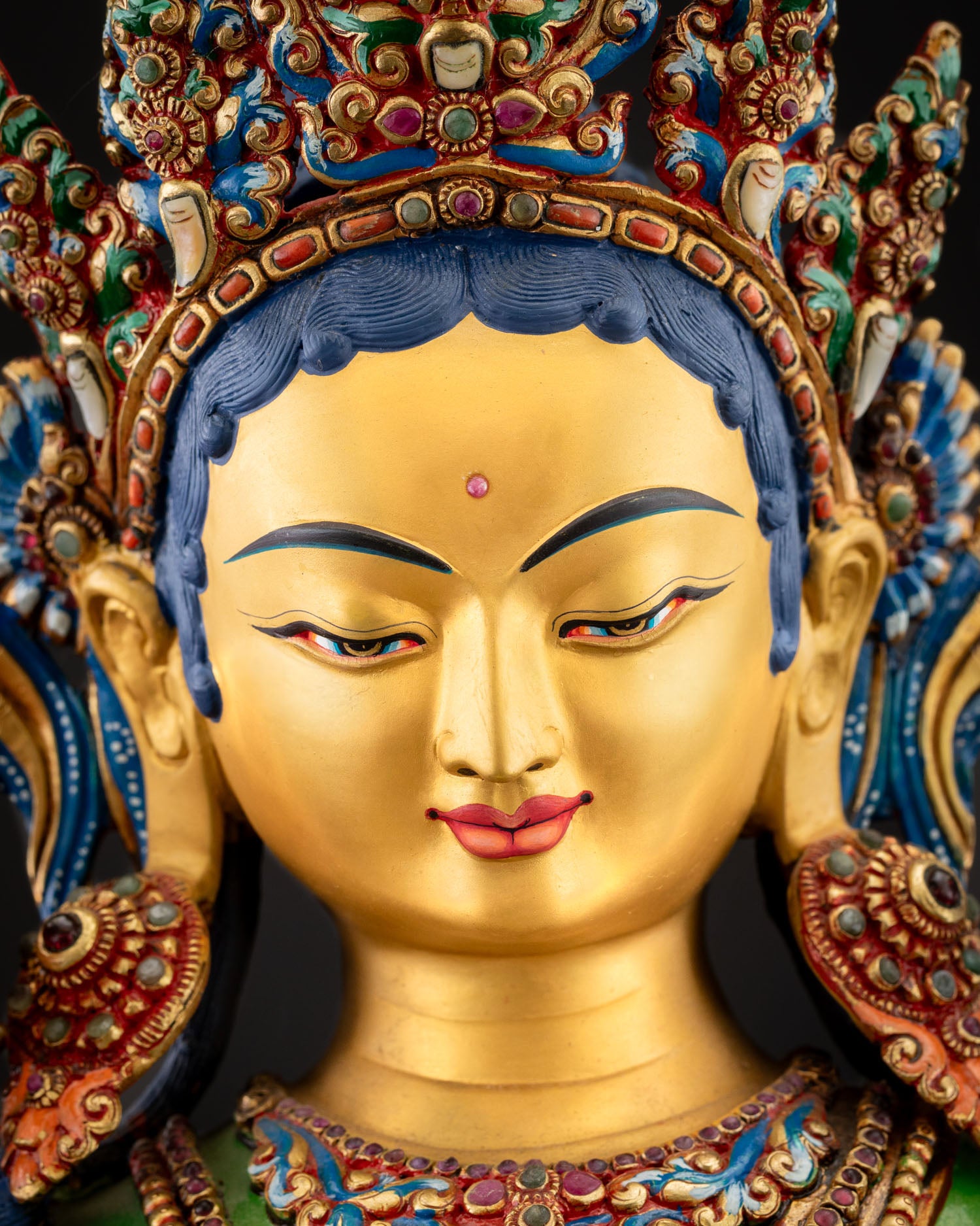 Close‑up of Green Tara face with gentle smile, gold paint, and urna on forehead