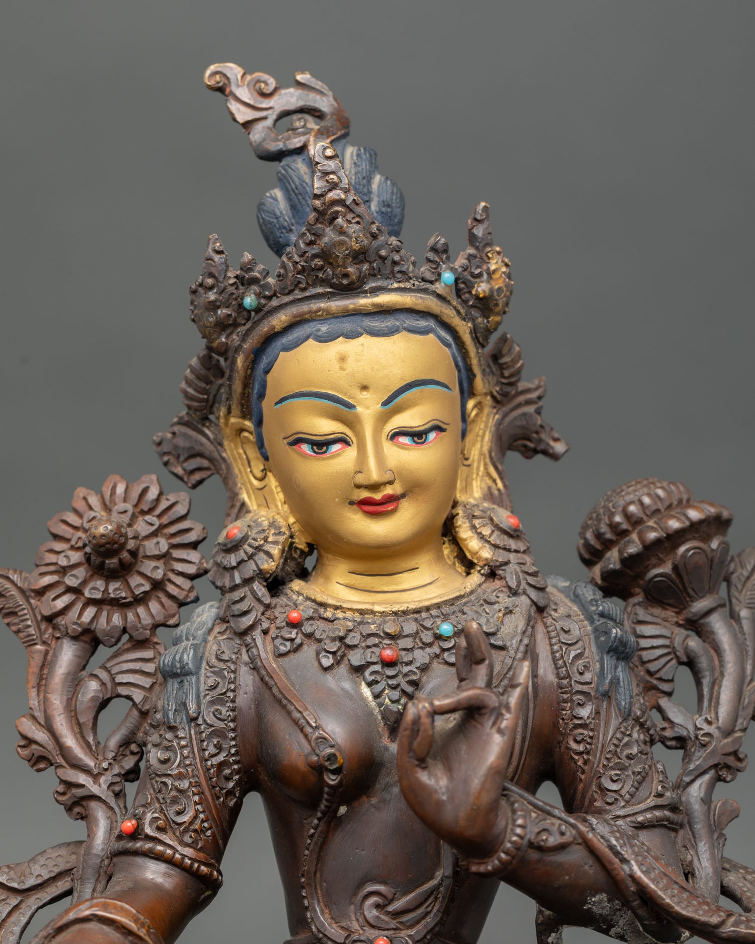 Close up of Green Tara gold painted face with oxidized copper finish and gemstone details.