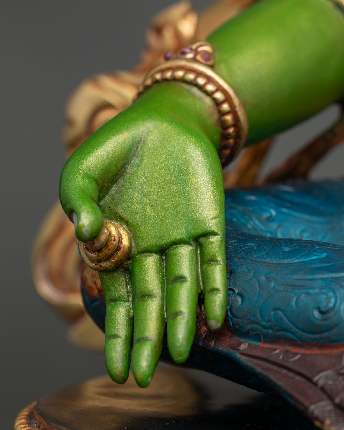 Close-up of Green Tara hand in varada mudra with gold bracelet and gemstone accents