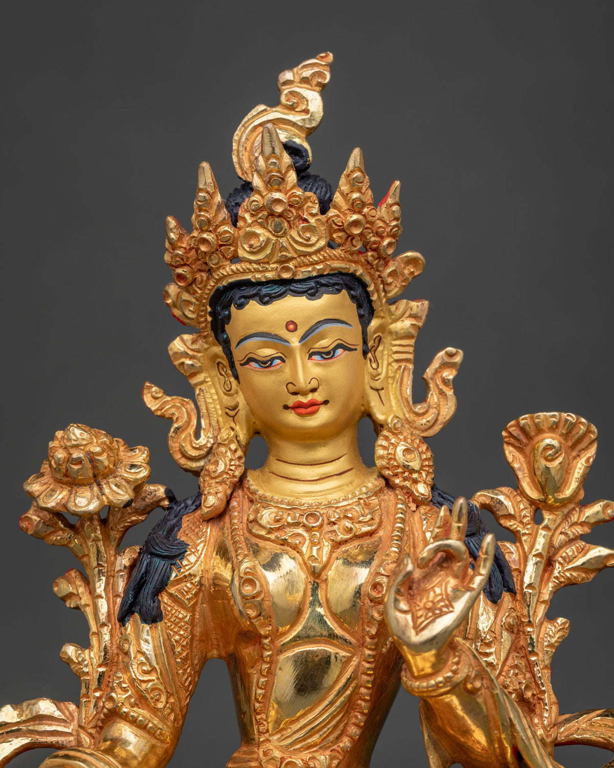 Close-up of Green Tara statue showing gilded face, ornate crown and lotus flower in hand