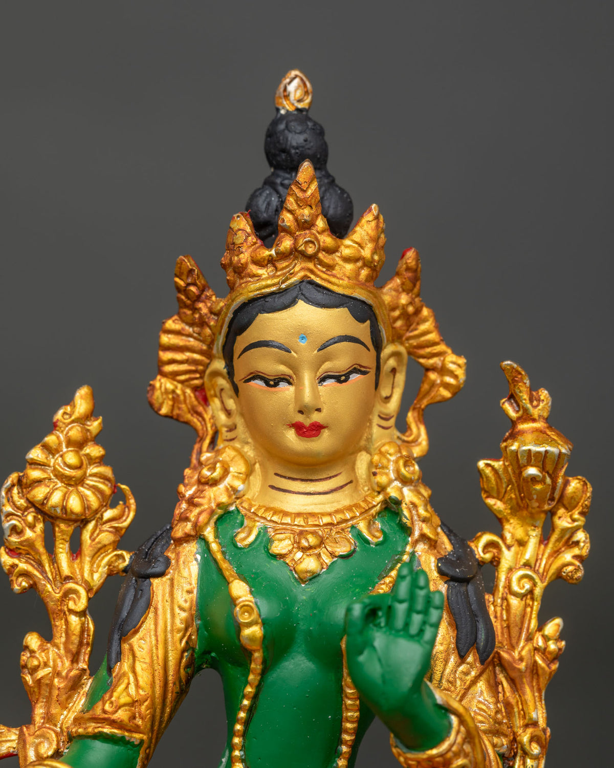 Close up of Green Tara statue with 24K gold painted face and gilded accents.