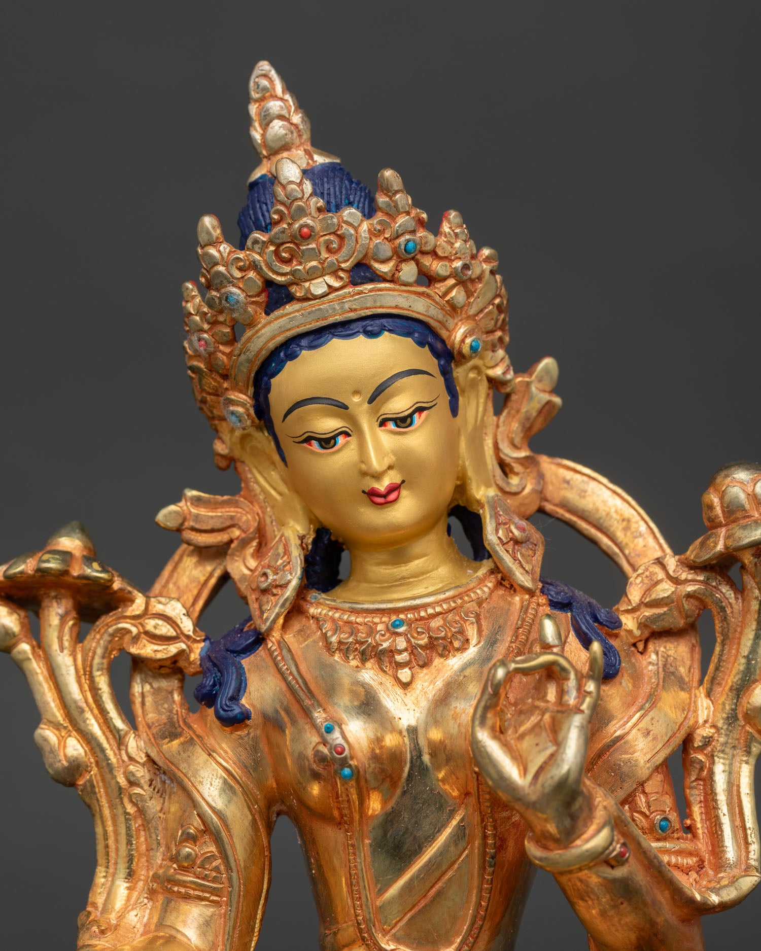 Close-up of Green Tara statue with 24K gold-painted face, turquoise coral inlays and serene expression.