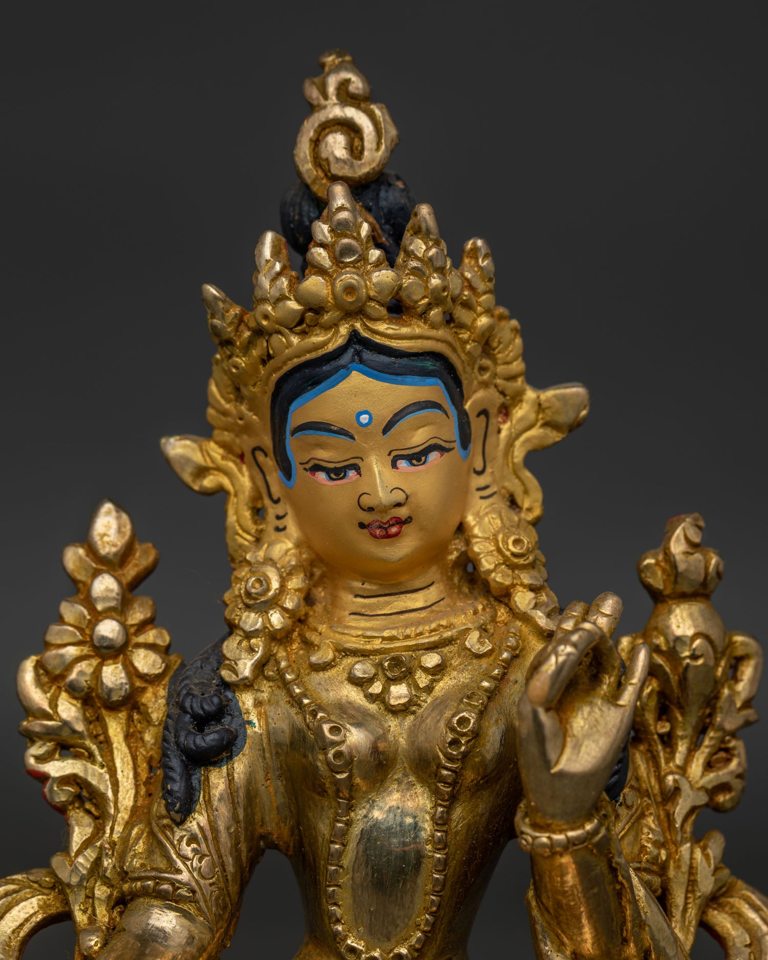 Close up of Green Tara statue with gold painted face and traditional Himalayan craftsmanship