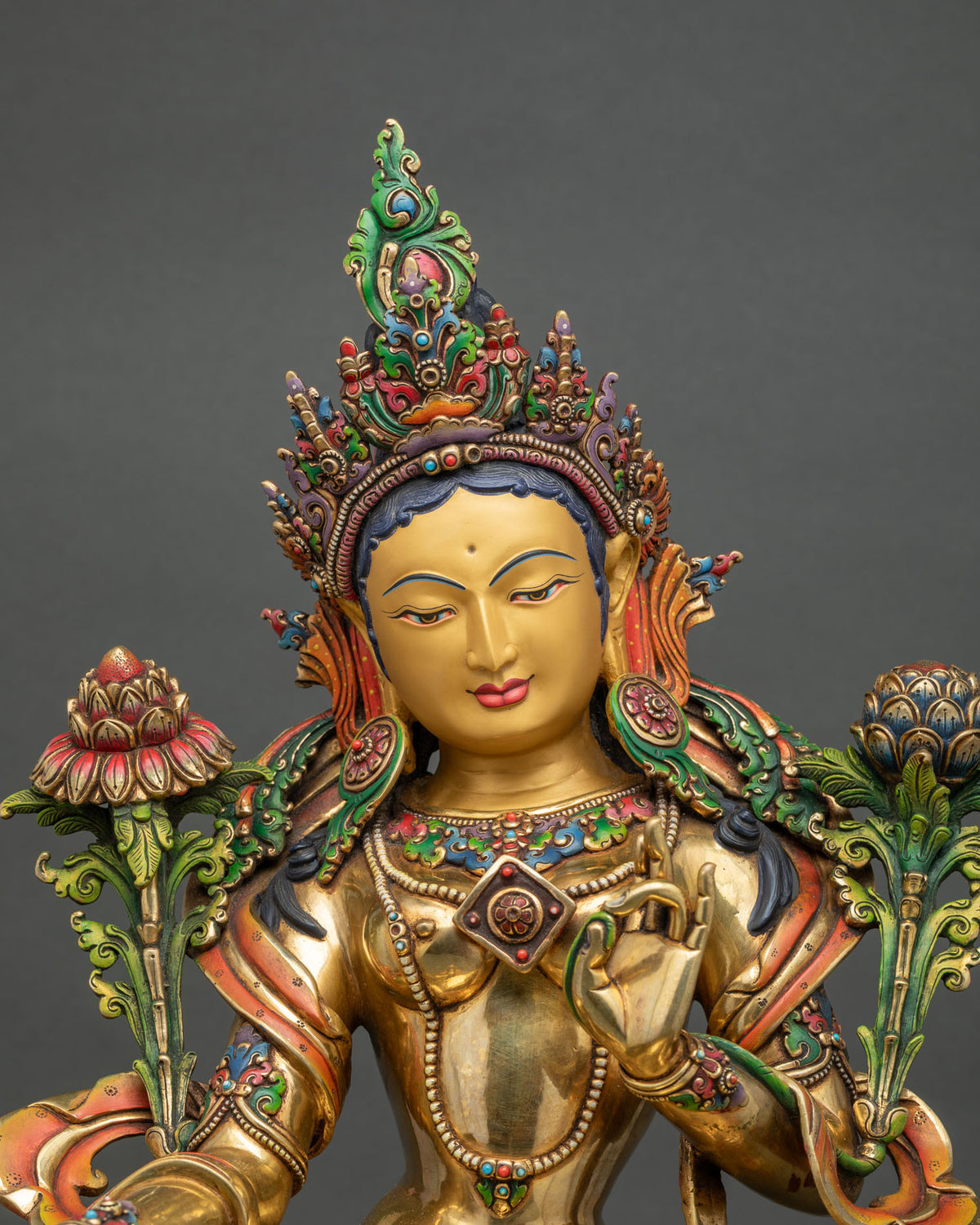 Close-up of Green Tara statue with jeweled crown, gold face and blooming utpala lotuses