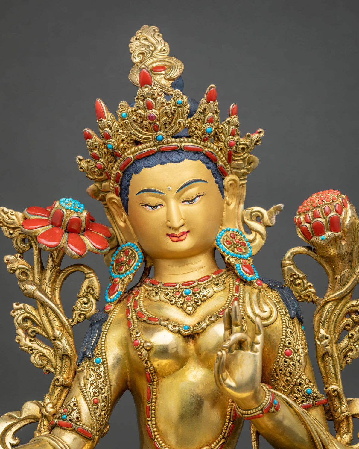 Close-up of Green Tara statue with jeweled crown, necklaces and blooming lotus stems in gold