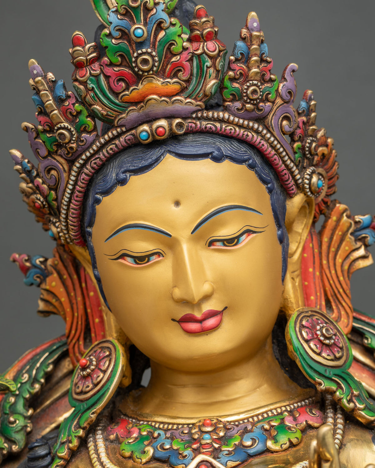 Close-up of Green Tara statue’s serene gold-painted face with downcast eyes and jeweled crown