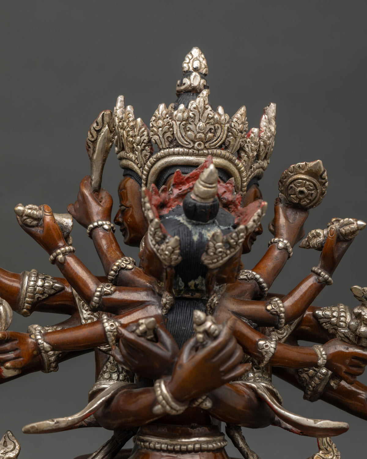 Close-up of Guhyasamaja statue’s multiple arms and ornate silver crown in oxidized copper