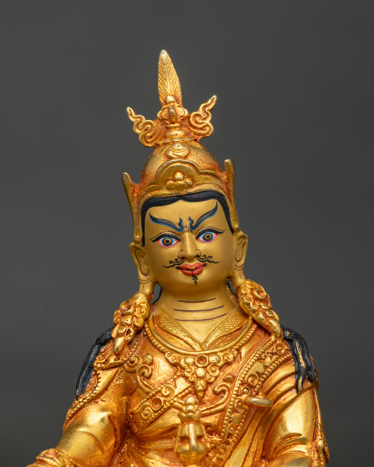 Close-up of Guru Rinpoche face with gold paint, black mustache and ornate feathered crown