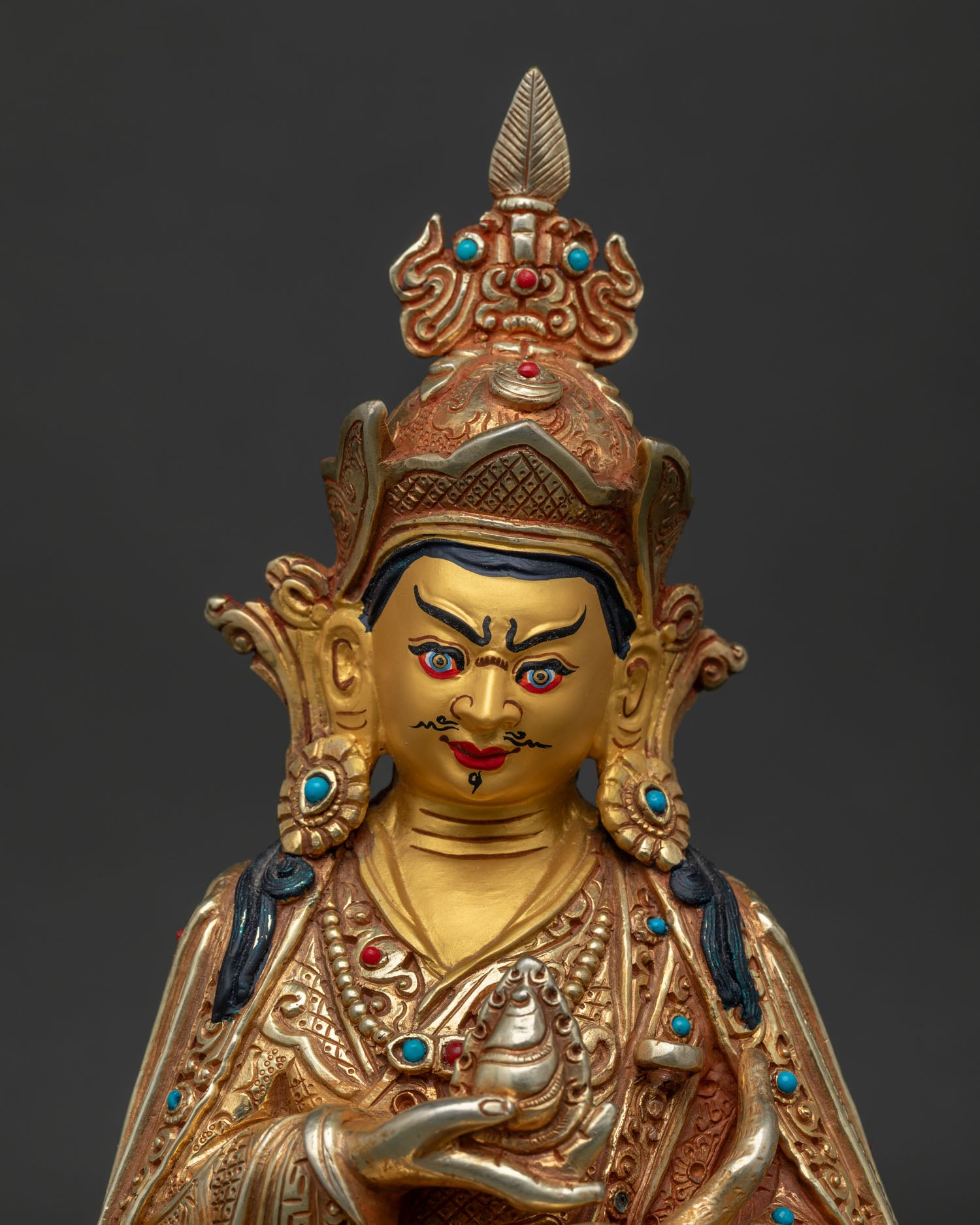 Close up of Guru Rinpoche face with red lotus hat vulture feather and gold gilded details.