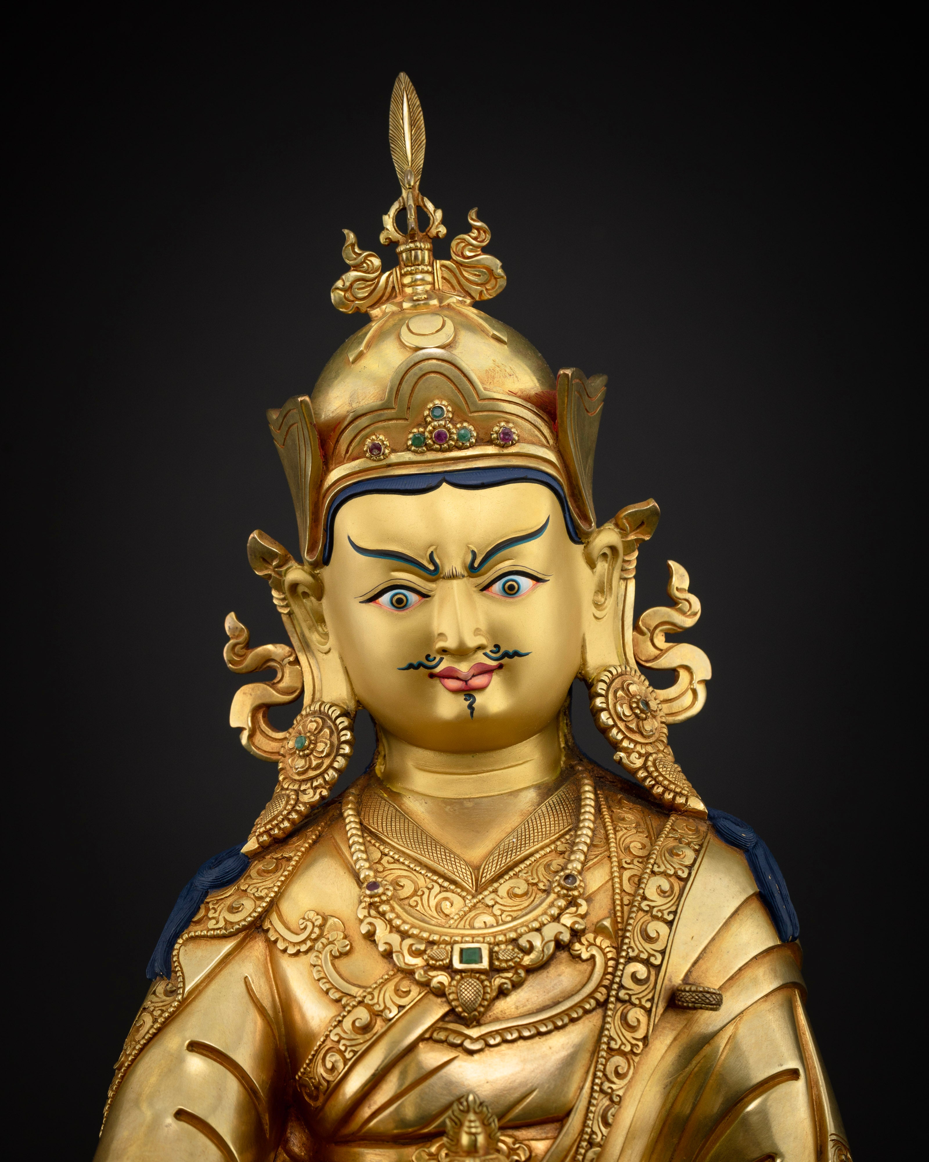 Close up of Guru Rinpoche sculpture with gold painted face and semi precious stone inlays