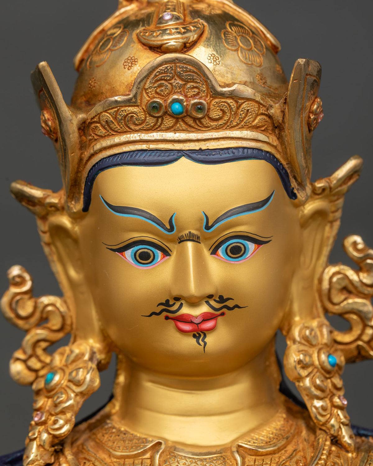 Close up of Guru Rinpoche statue face with 24K gold paint and semi-wrathful expression