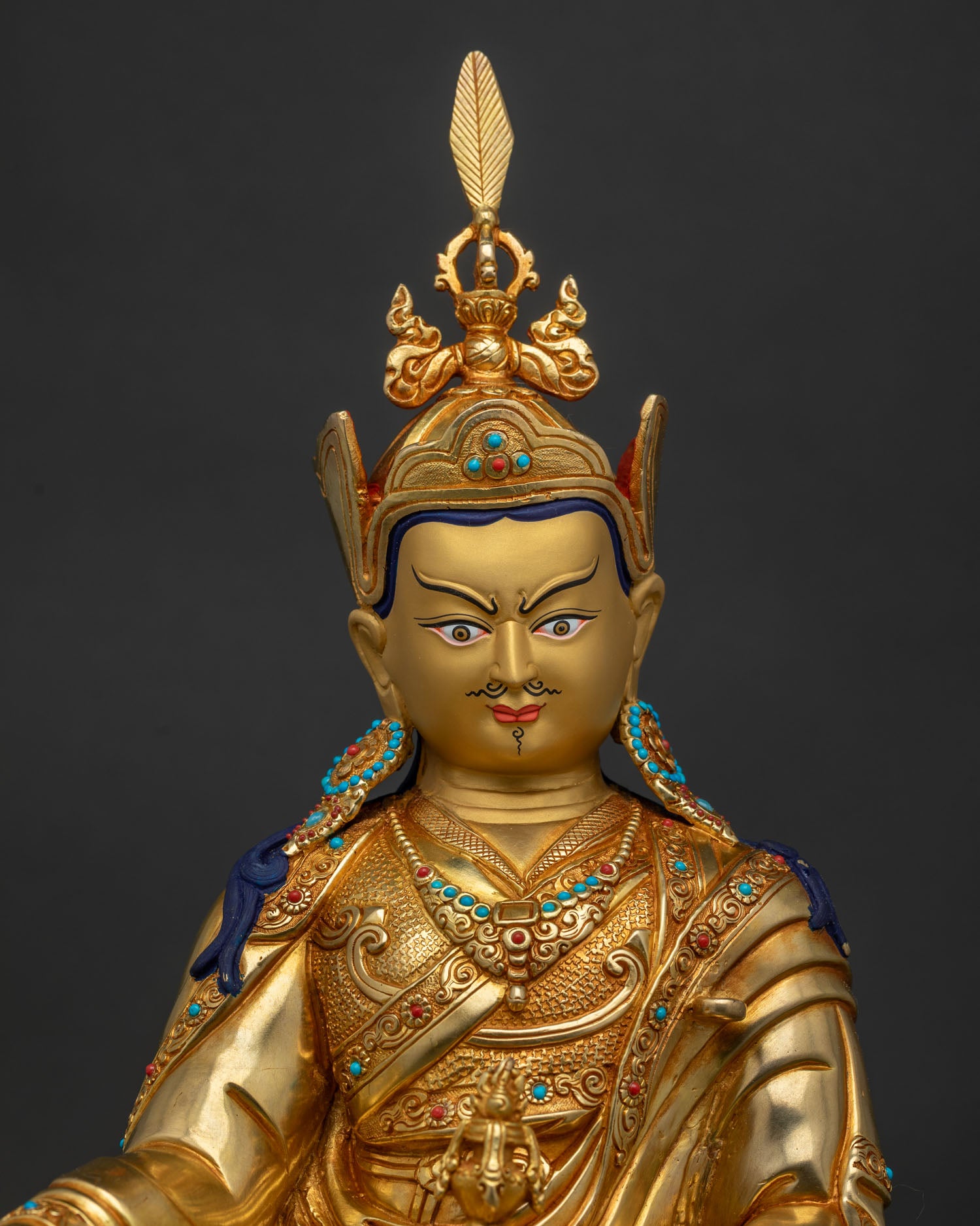 Close up of Guru Rinpoche Statue with gold painted face turquoise coral stones and red lotus hat