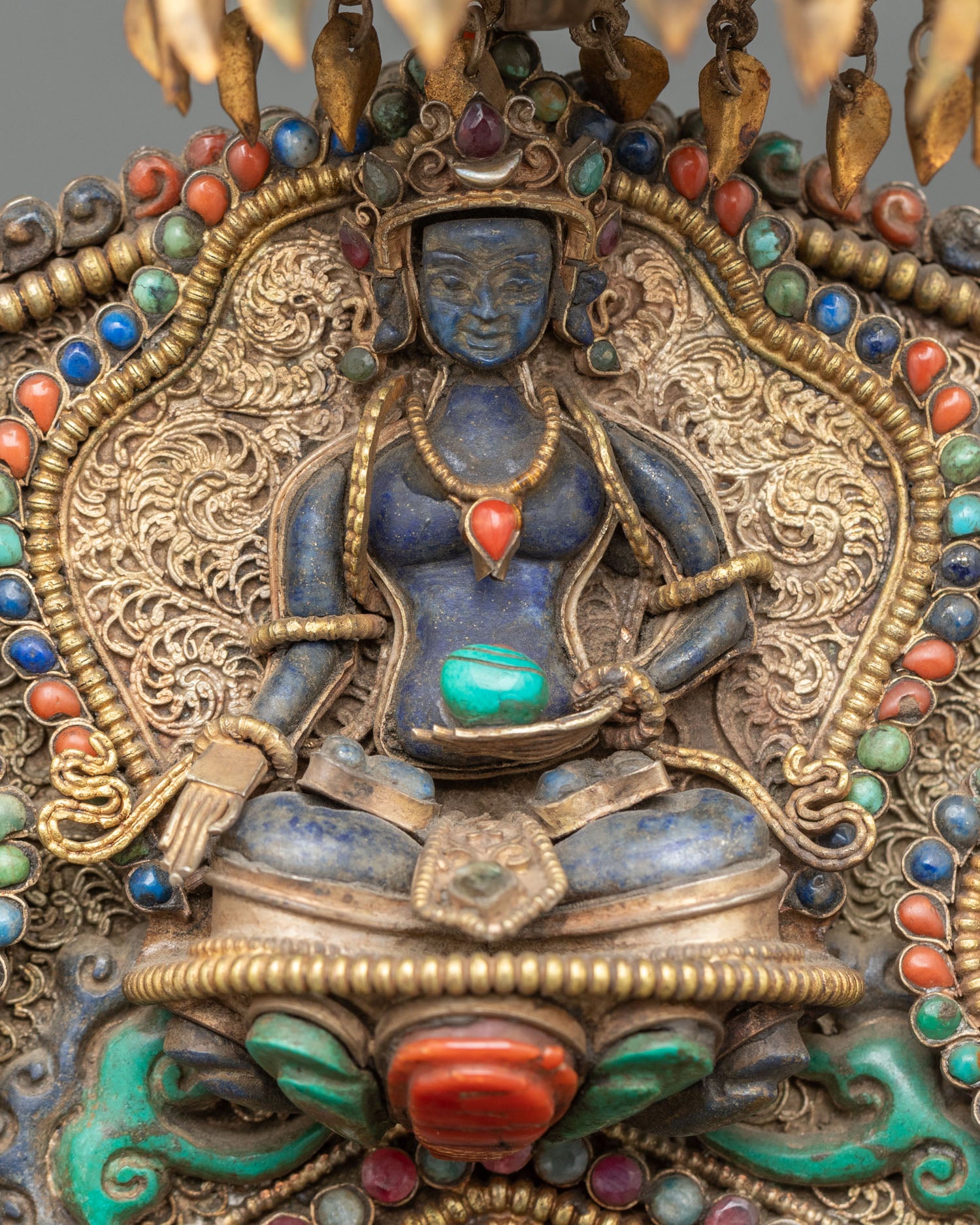 close-up of lapis lazuli Buddha attendant in halo, deep blue stone figure framed by gold filigree and turquoise accents