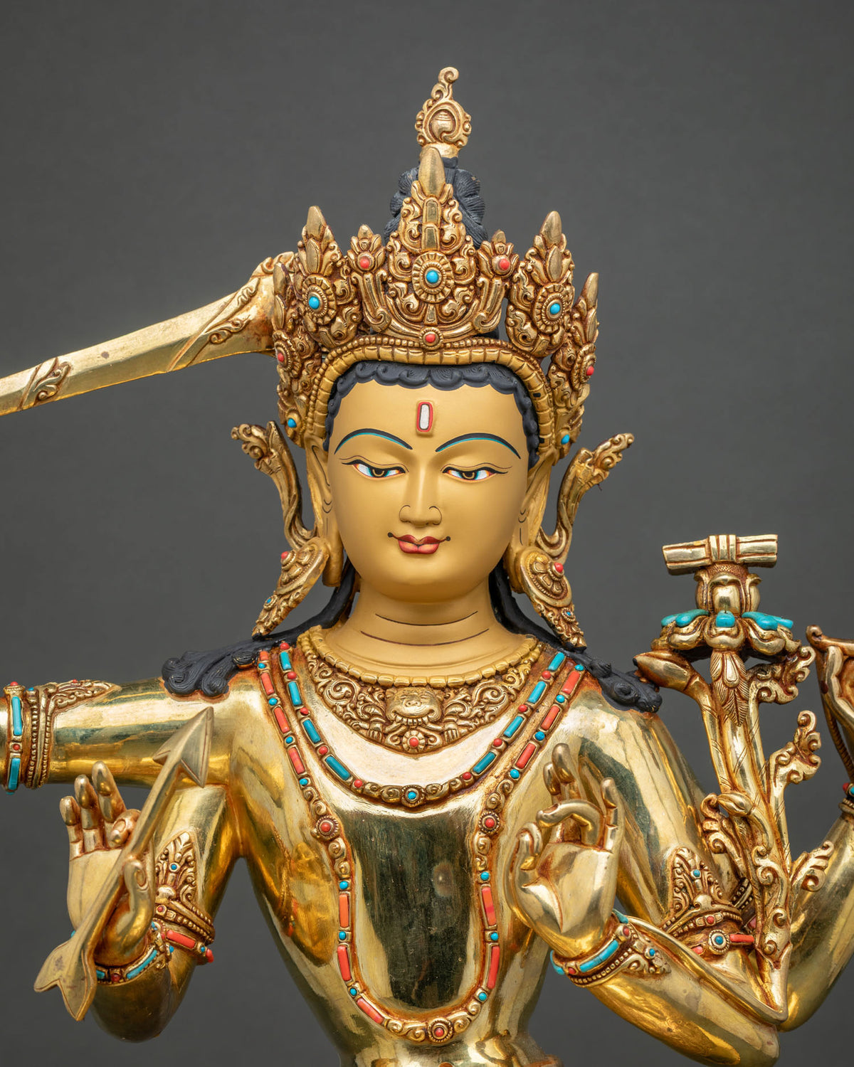 Close-up of Maha Manjushri statue with jeweled crown, flaming sword and utpala with turquoise inlays