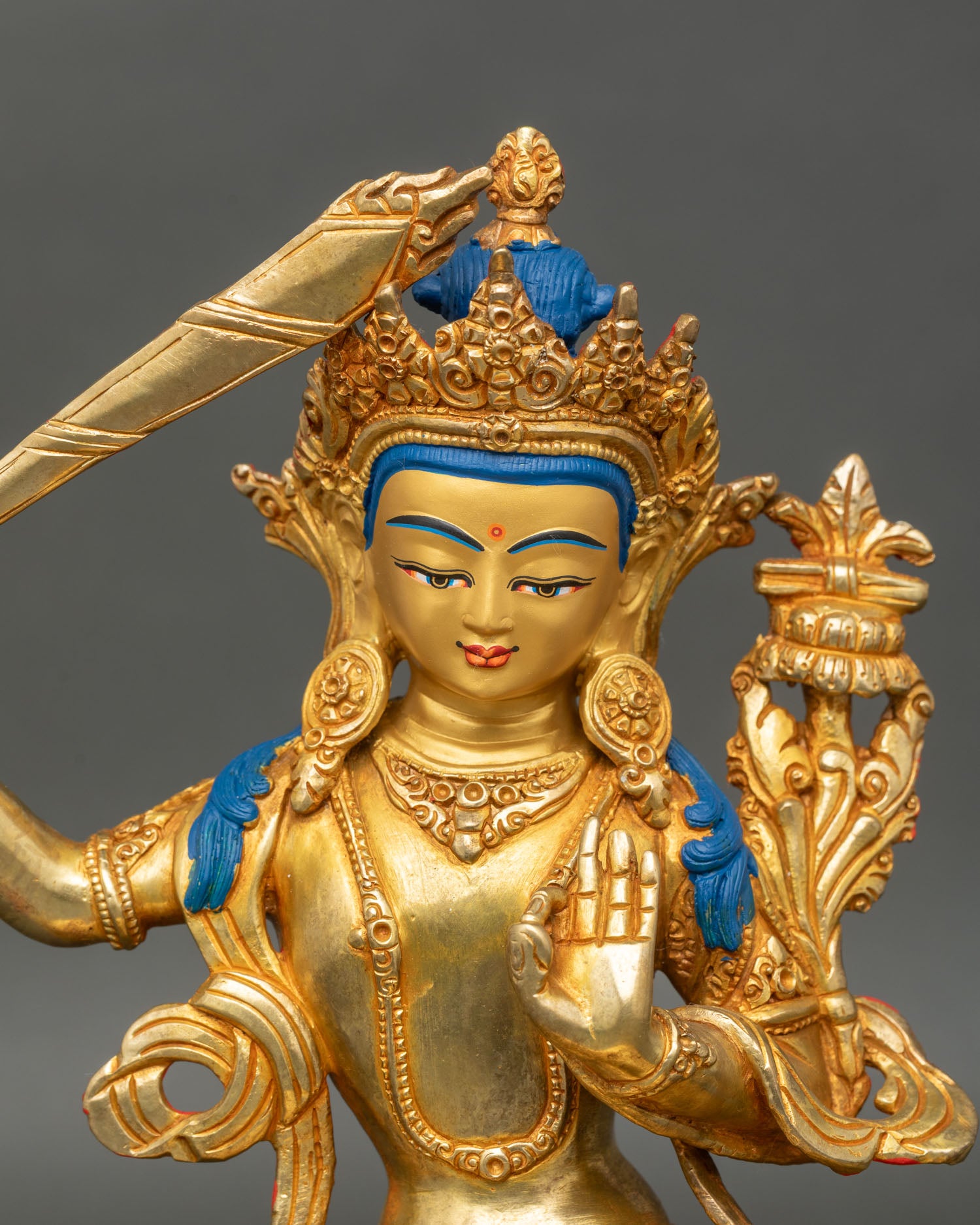 Close up of Manjushri’s face, gold-painted with a serene expression and intricate carvings.