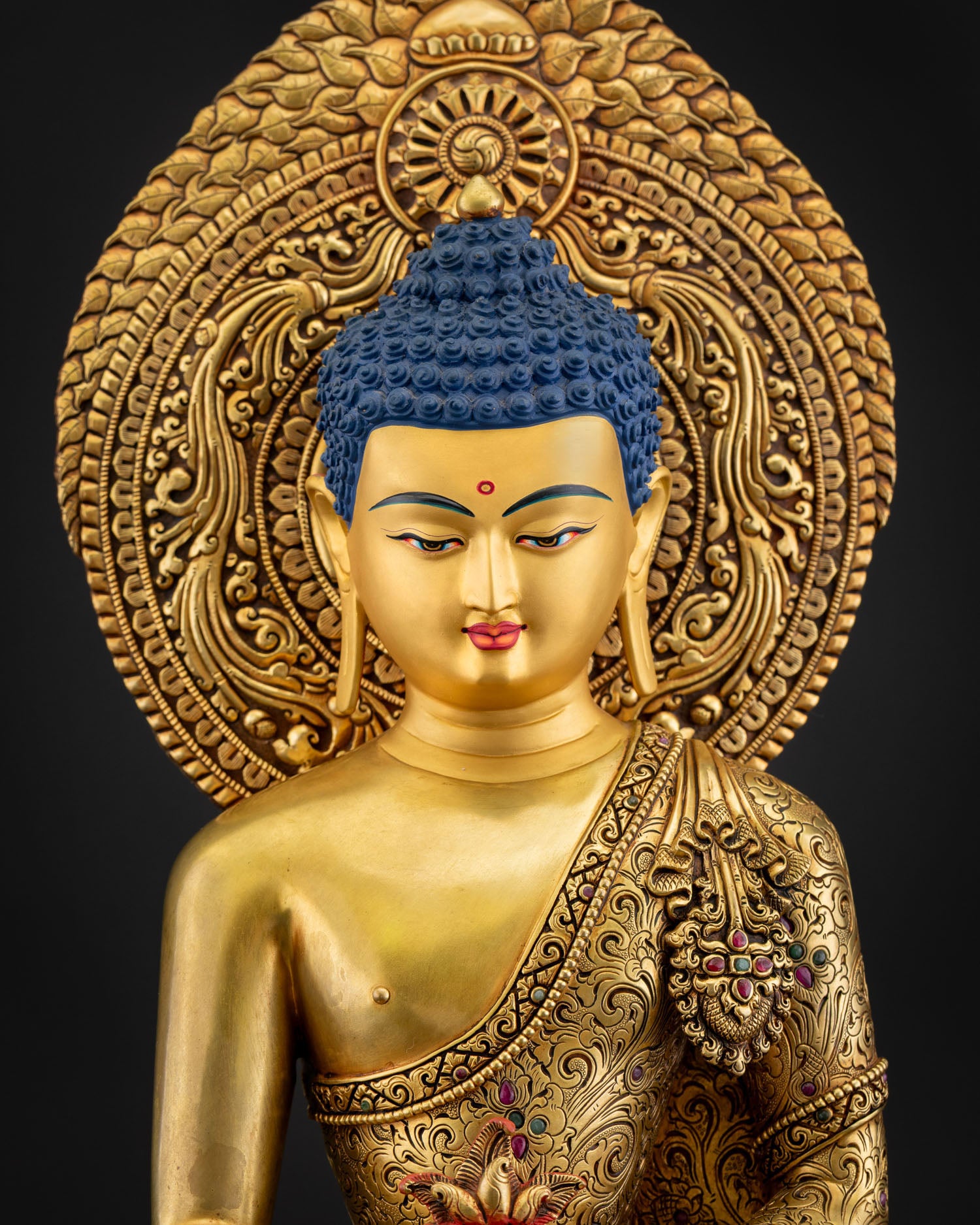 Close up of Medicine Buddha statue showing intricate repoussé robe details, semi-precious stones