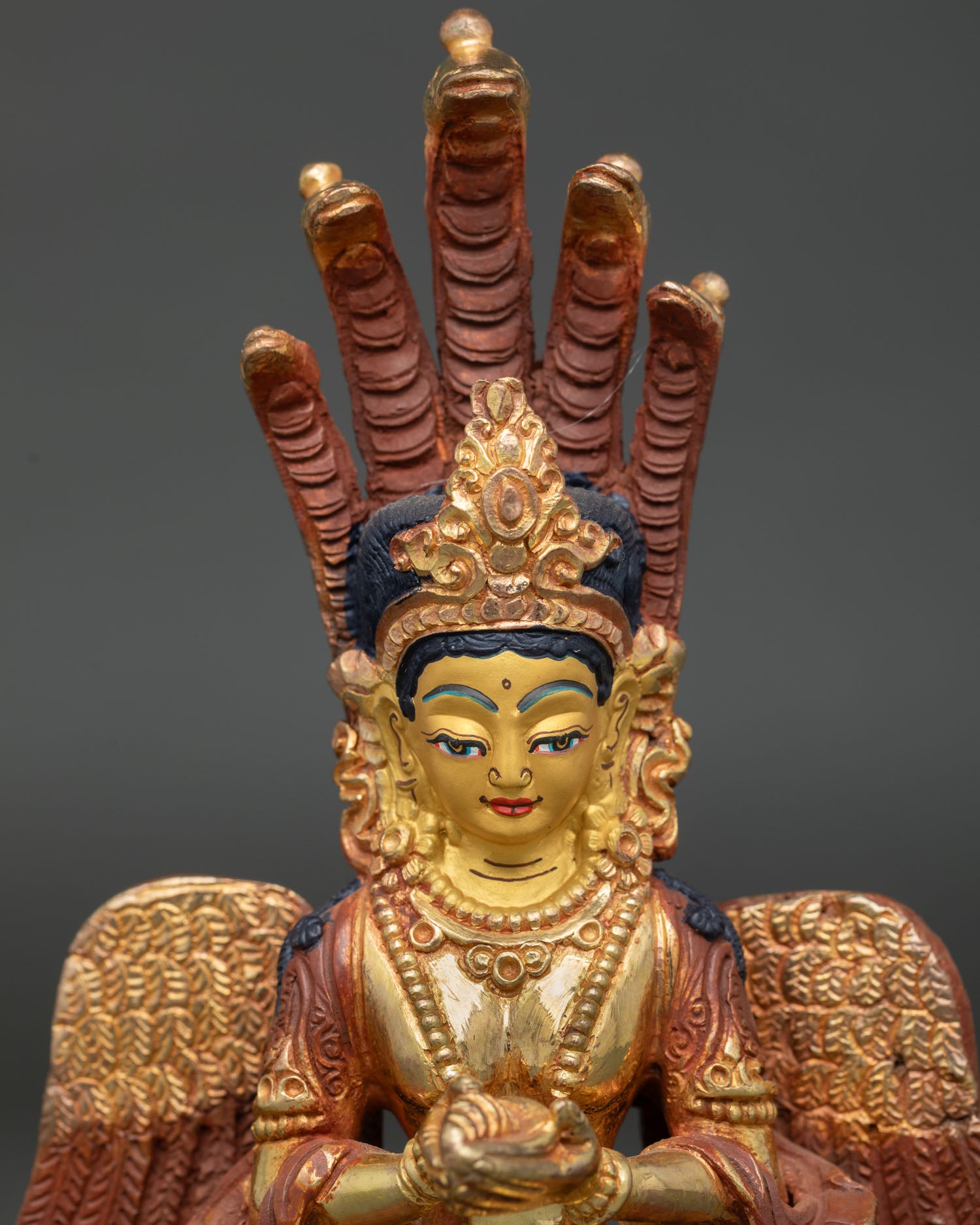 Close-up of Naga Kanya statue with five serpent crown, gold-painted face and conch shell.