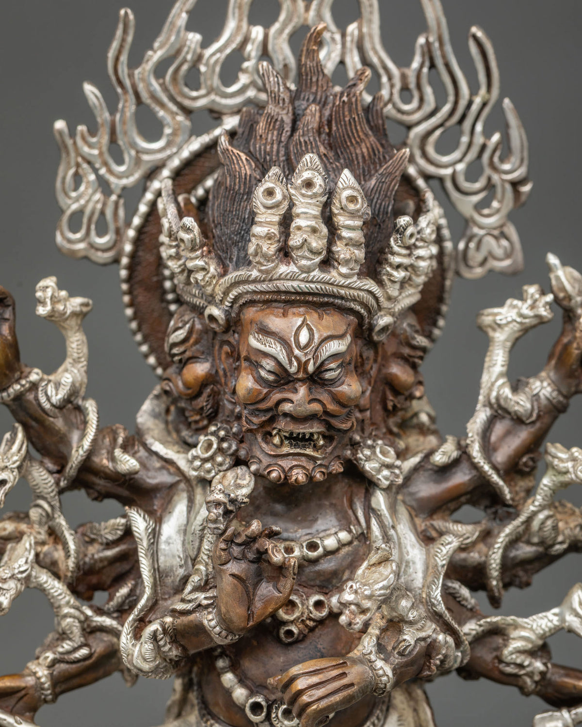 Close-up of oxidized copper Ucchusma statue showing wrathful face, multiple arms and silver detailing