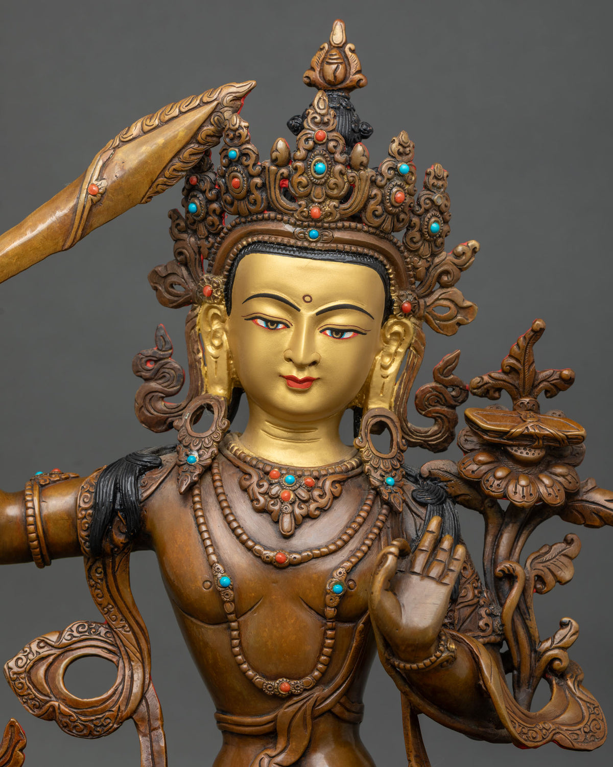 Close up of oxidized Manjushri copper statue with crown, flaming sword and lotus stem