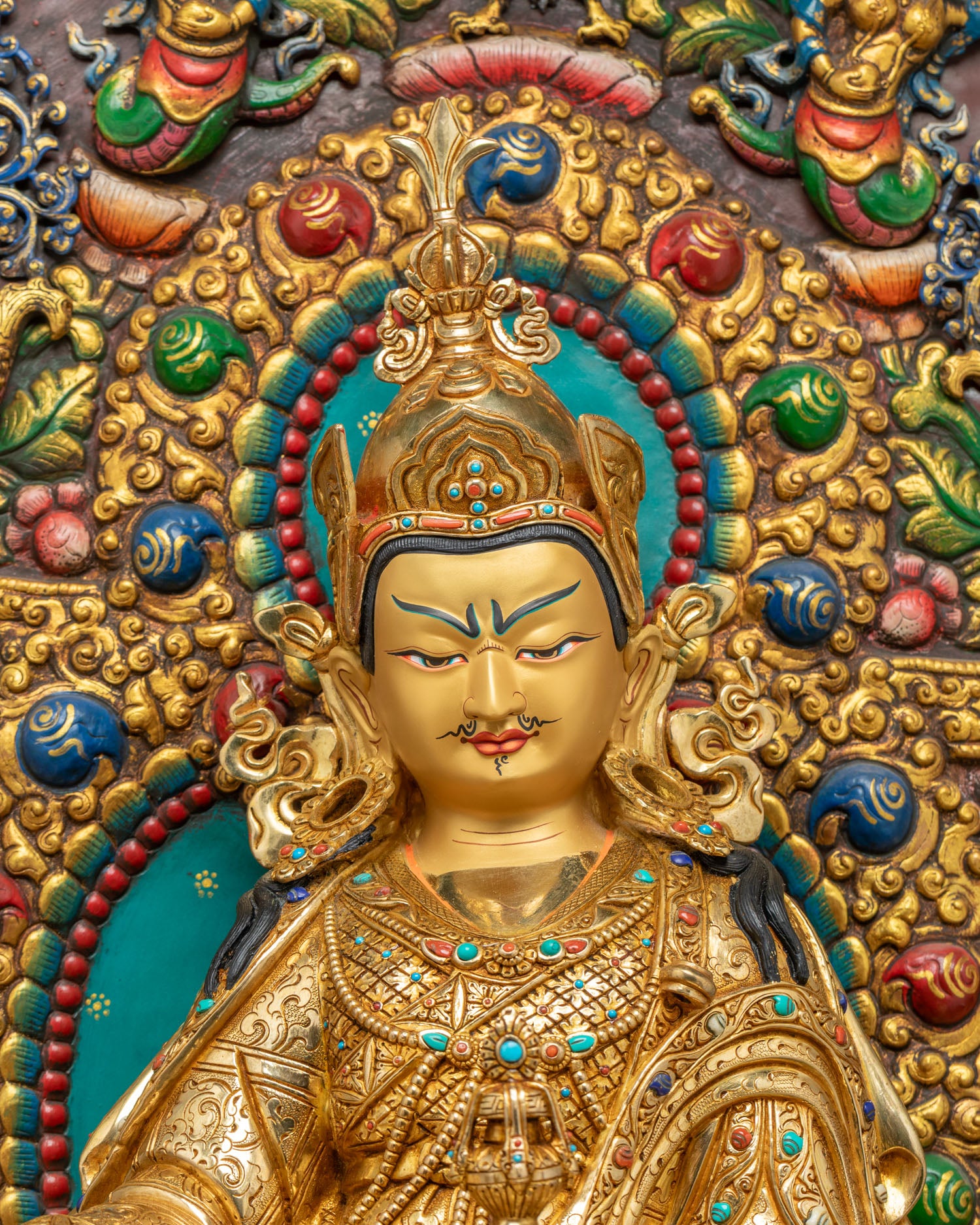Close-up of Padmasambhava's gold-painted face and crown on Guru Rinpoche statue