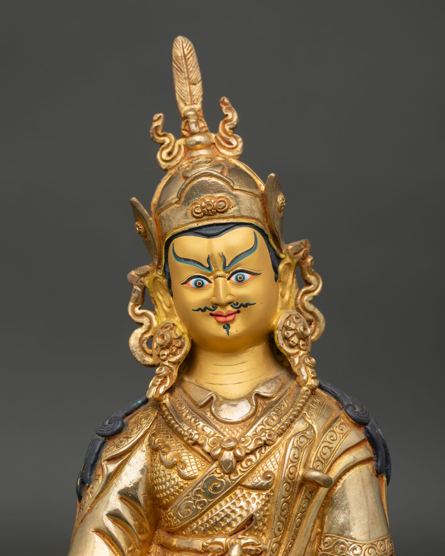 Close up of Padmasambhava Guru Rinpoche gold painted face with ornate crown and jewelry details