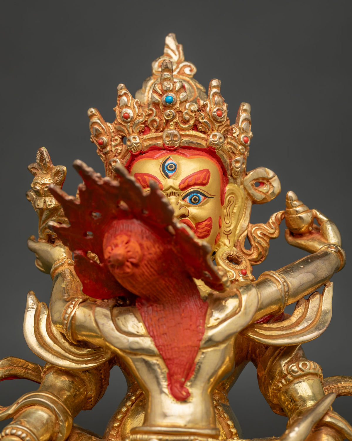 Close-up of Red Dzambhala Marpo statue showing gilded crown, consort and seated lotus base