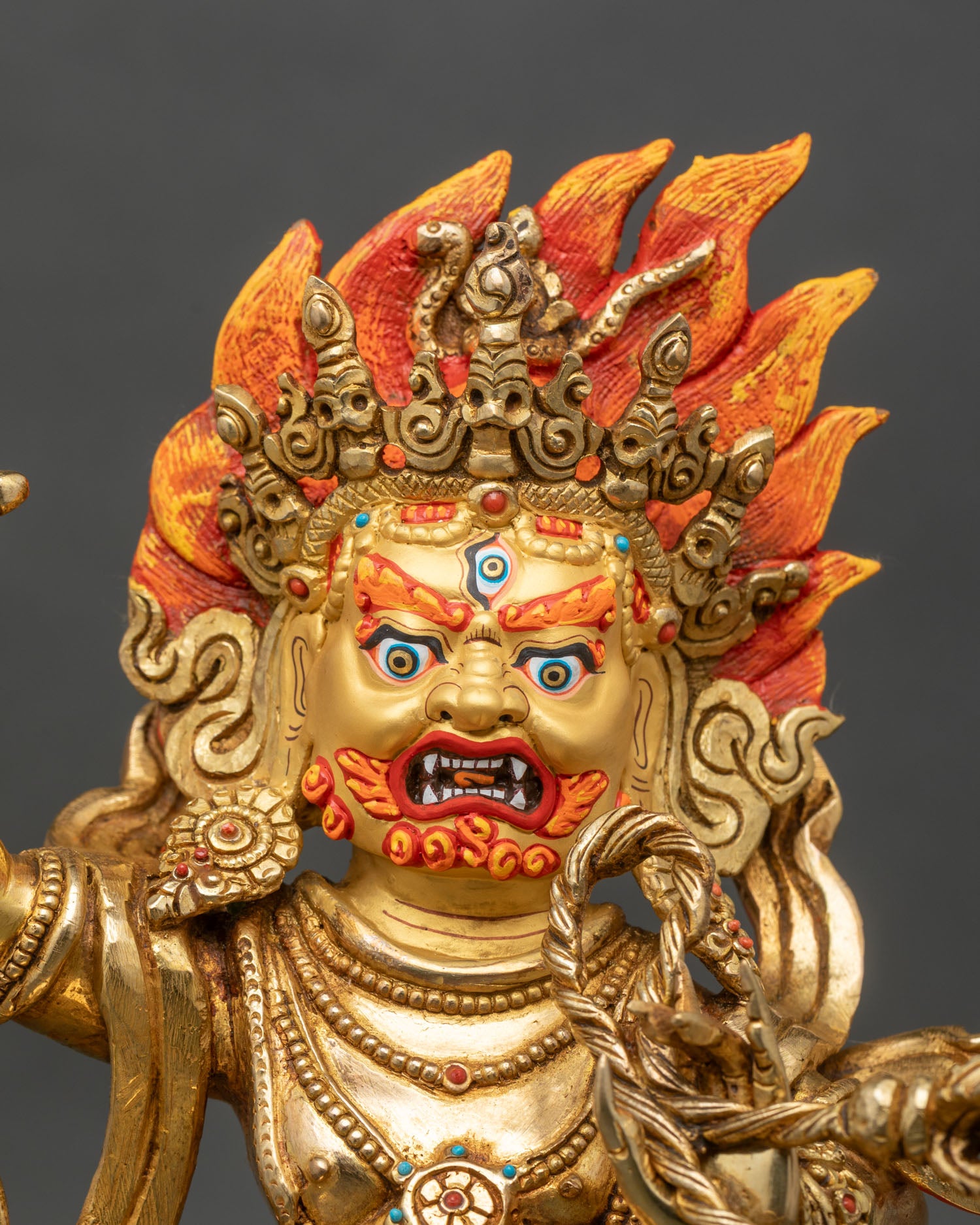 Close up of Vajrapani statue showing gold finish, vajra hand gesture and flame aureole