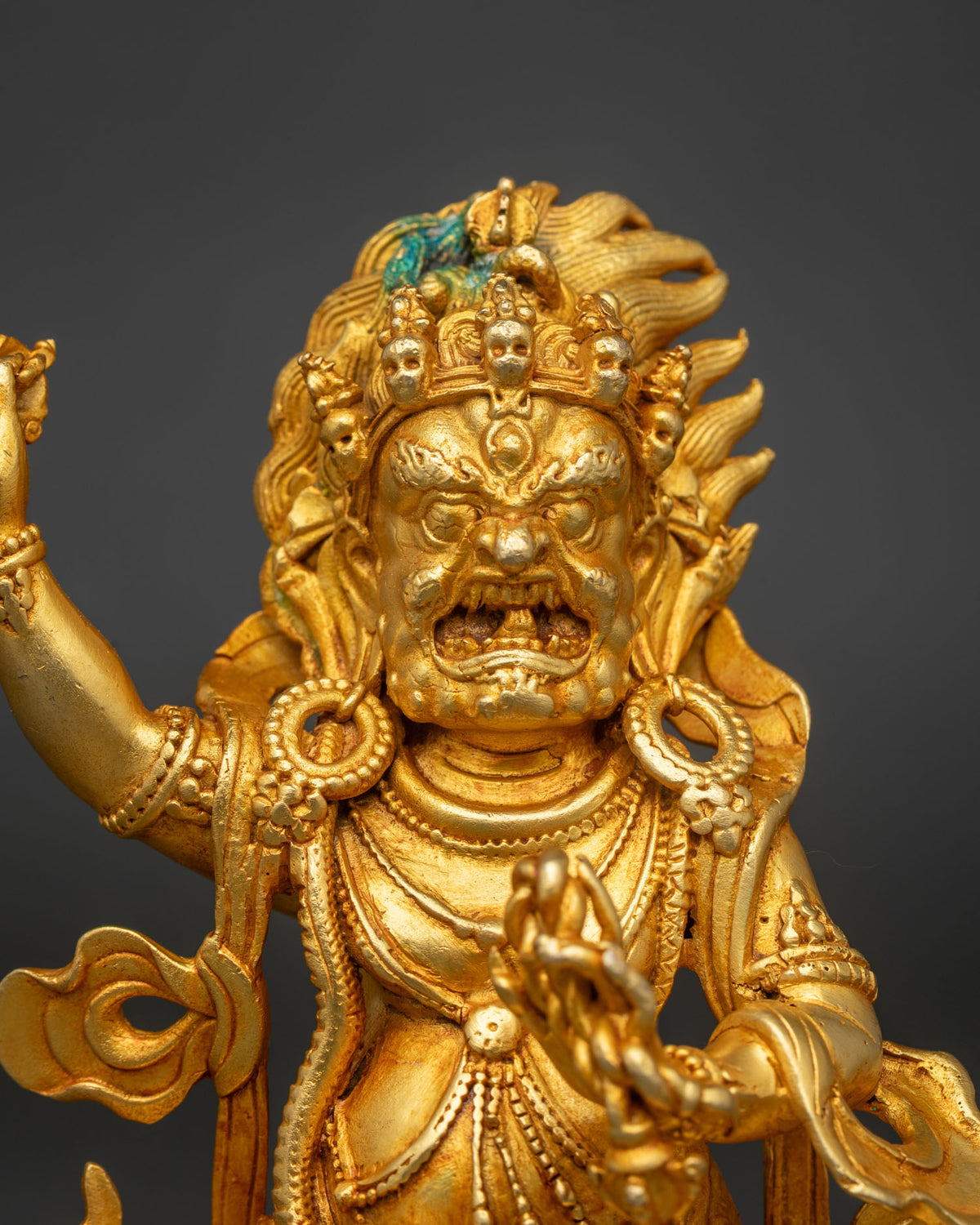 Close-up of Vajrapani statue’s wrathful face, skull crown and gold fire-gilded ornaments