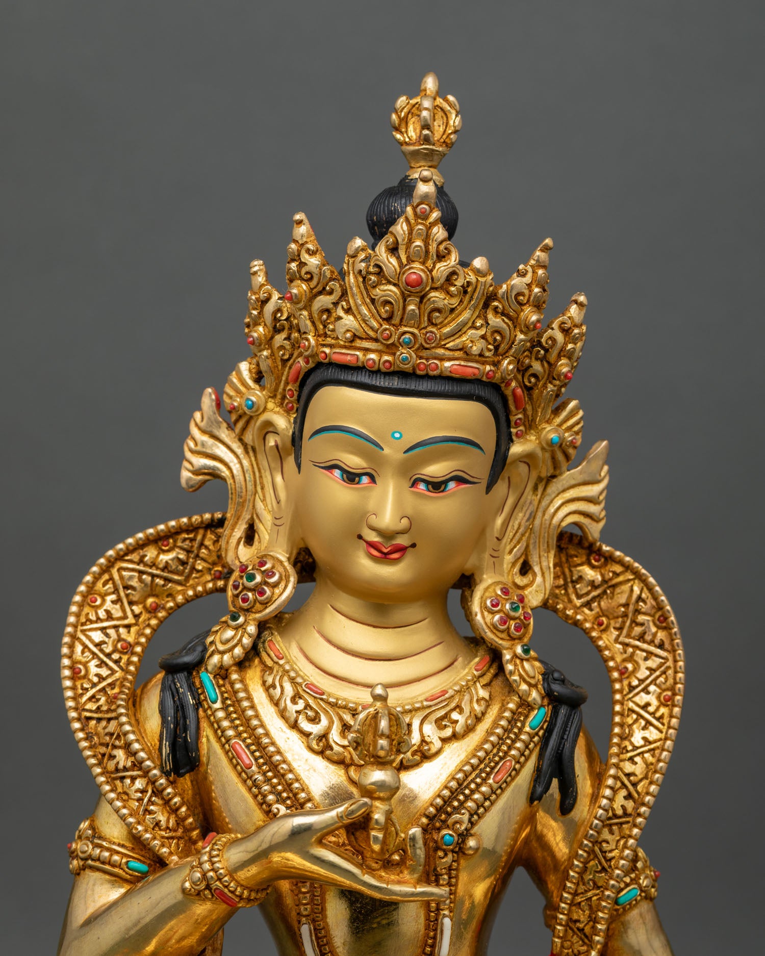 Close up of Vajrasattva gold-painted face holding Vajra and bell with semi-precious stones
