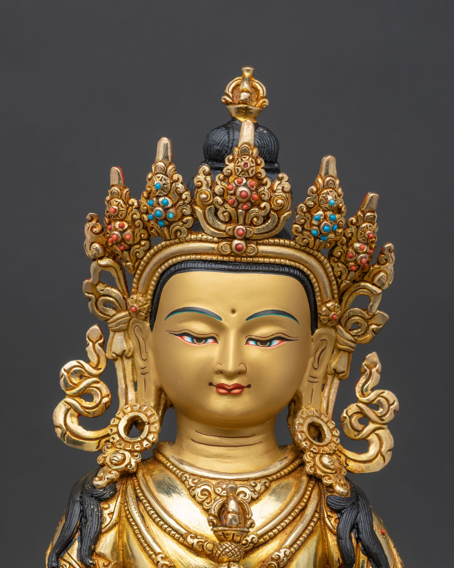 Close up of Vajrasattva gold-painted face holding vajra and bell with stone inlays