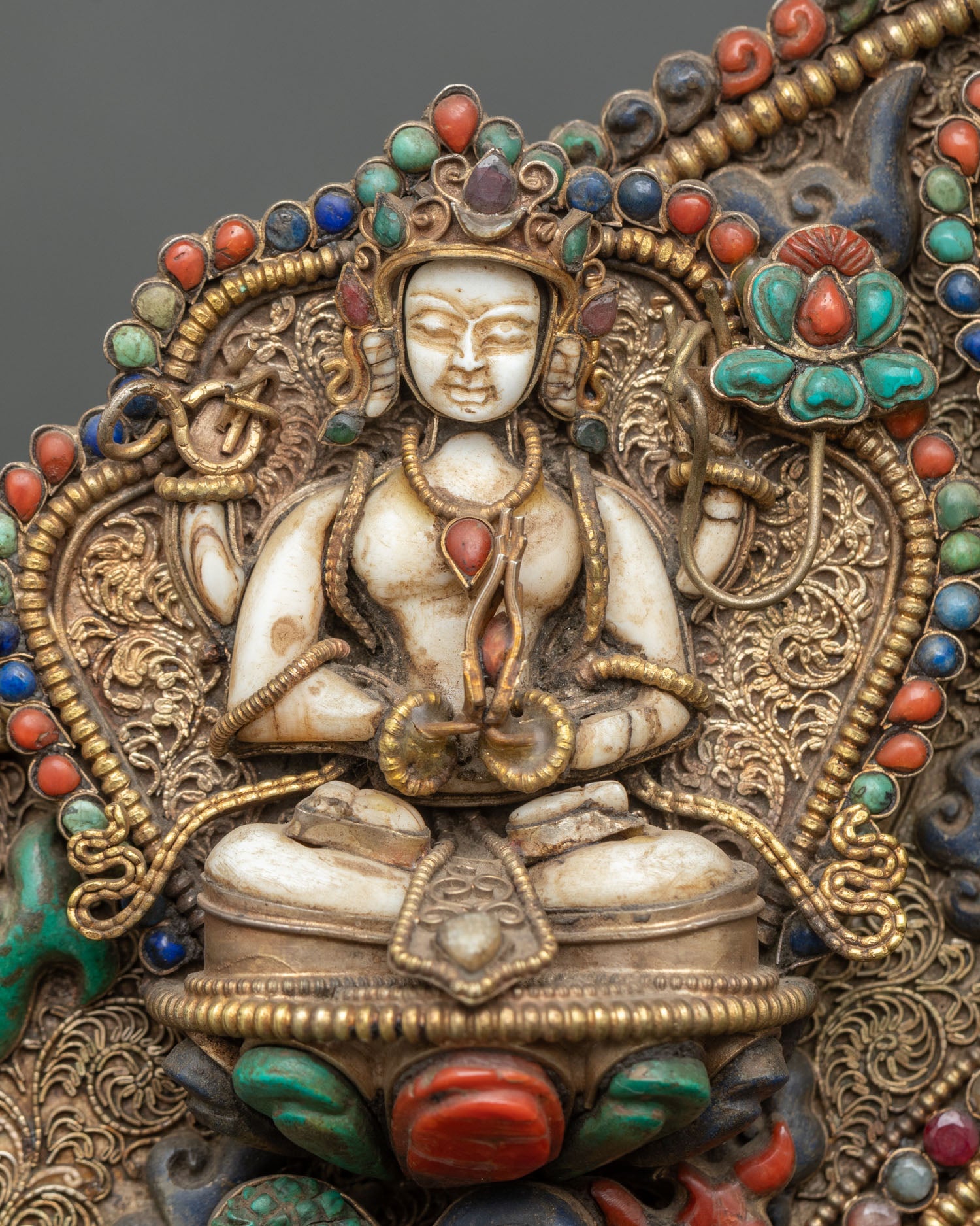 Close-up of white stone Chenrezig attendant within halo, intricate carving and gold-gilded filigree