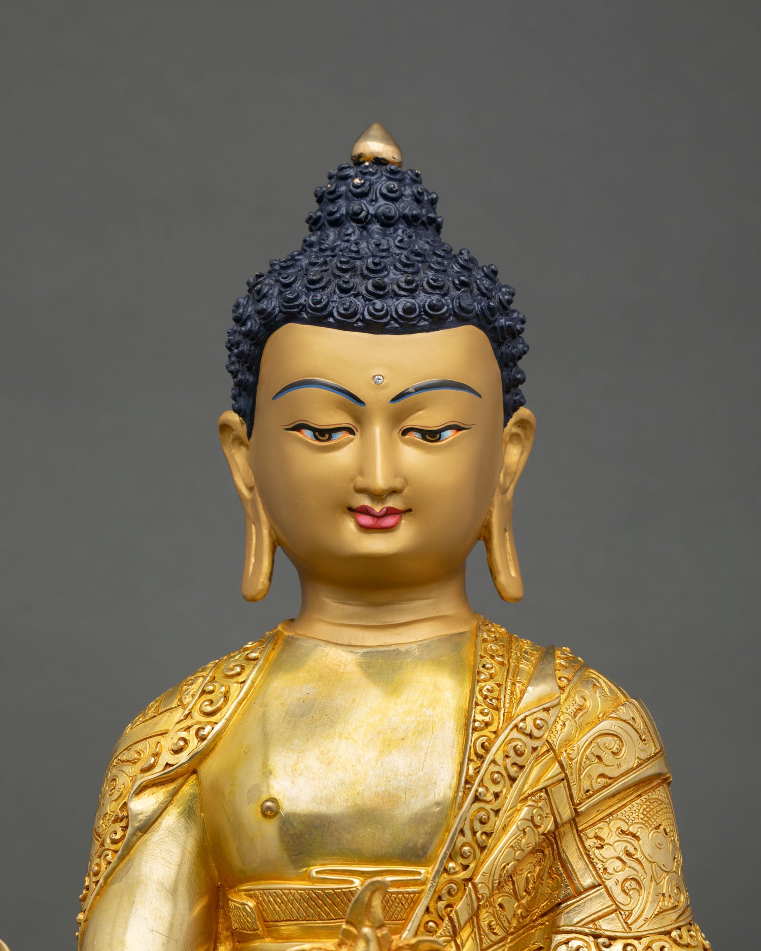 Close up view of Bhaisajyaguru Medicine Buddha sculpture showing gold painted face detailed robes