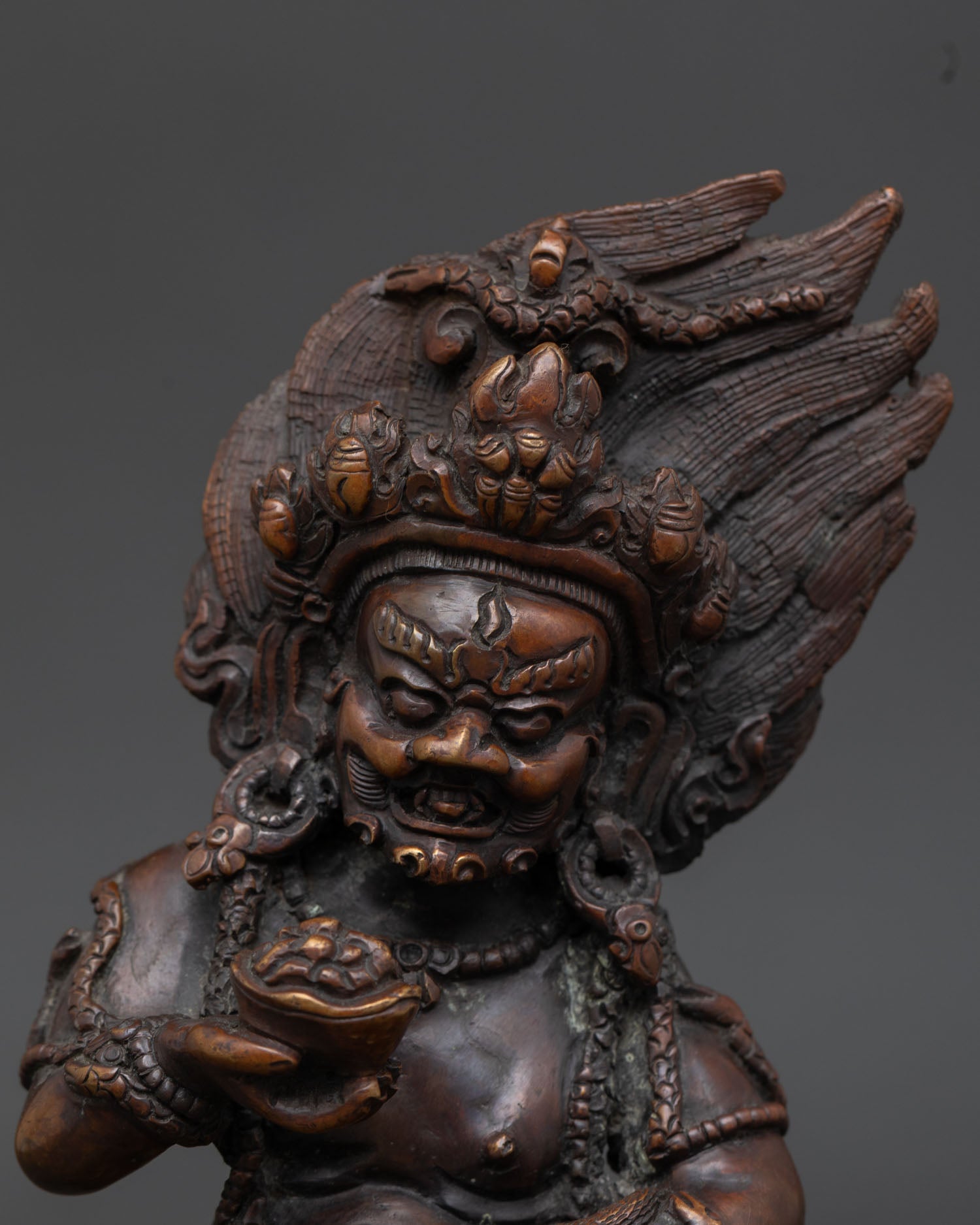 Close up view of Black Dzambhala statue showing fierce expression, jewel spitting mongoose, oxidized copper finish