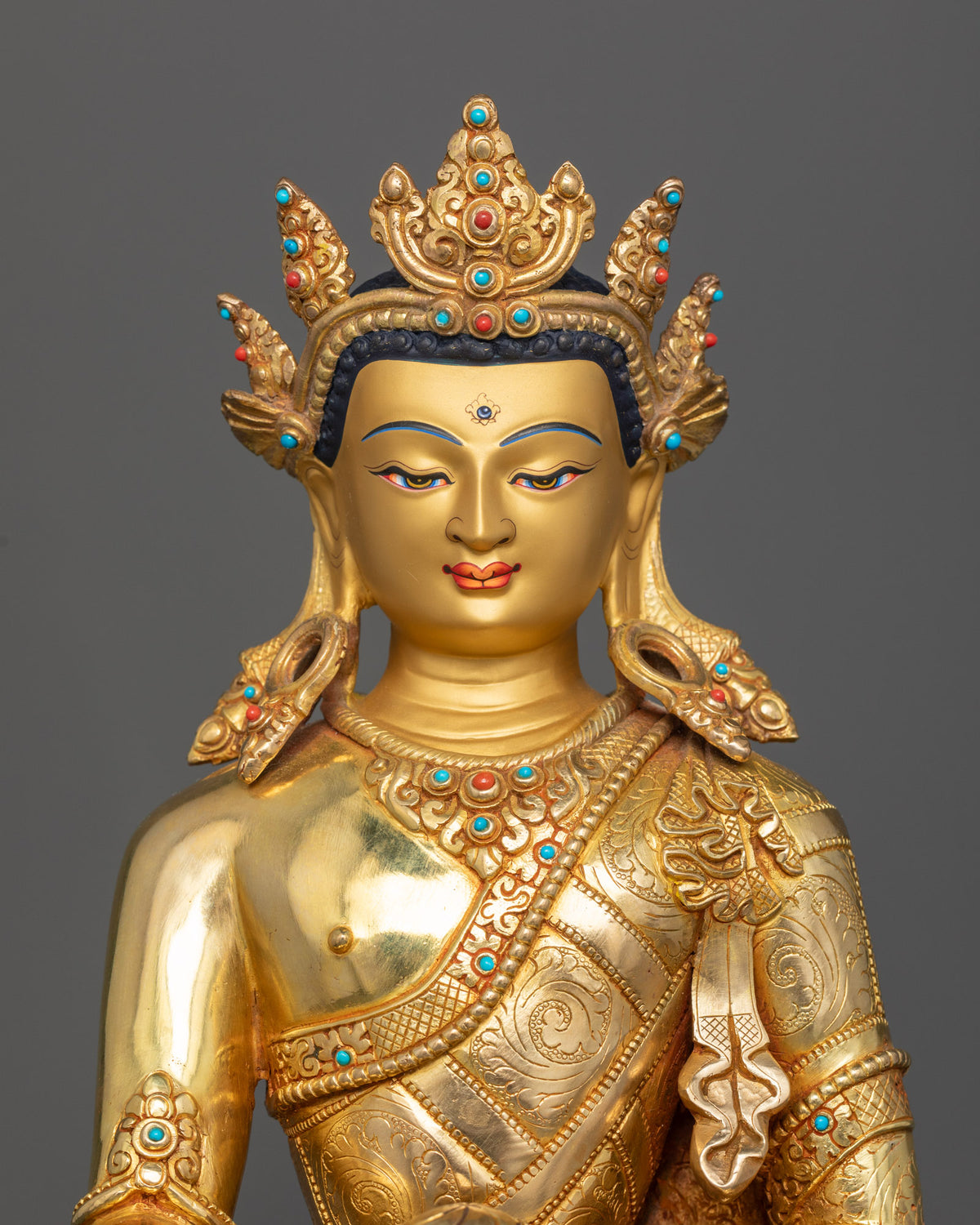 Close-up view of crowned Buddha Shakyamuni statue featuring a serene gold-painted face, ornate crown, and semi-precious gemstone details