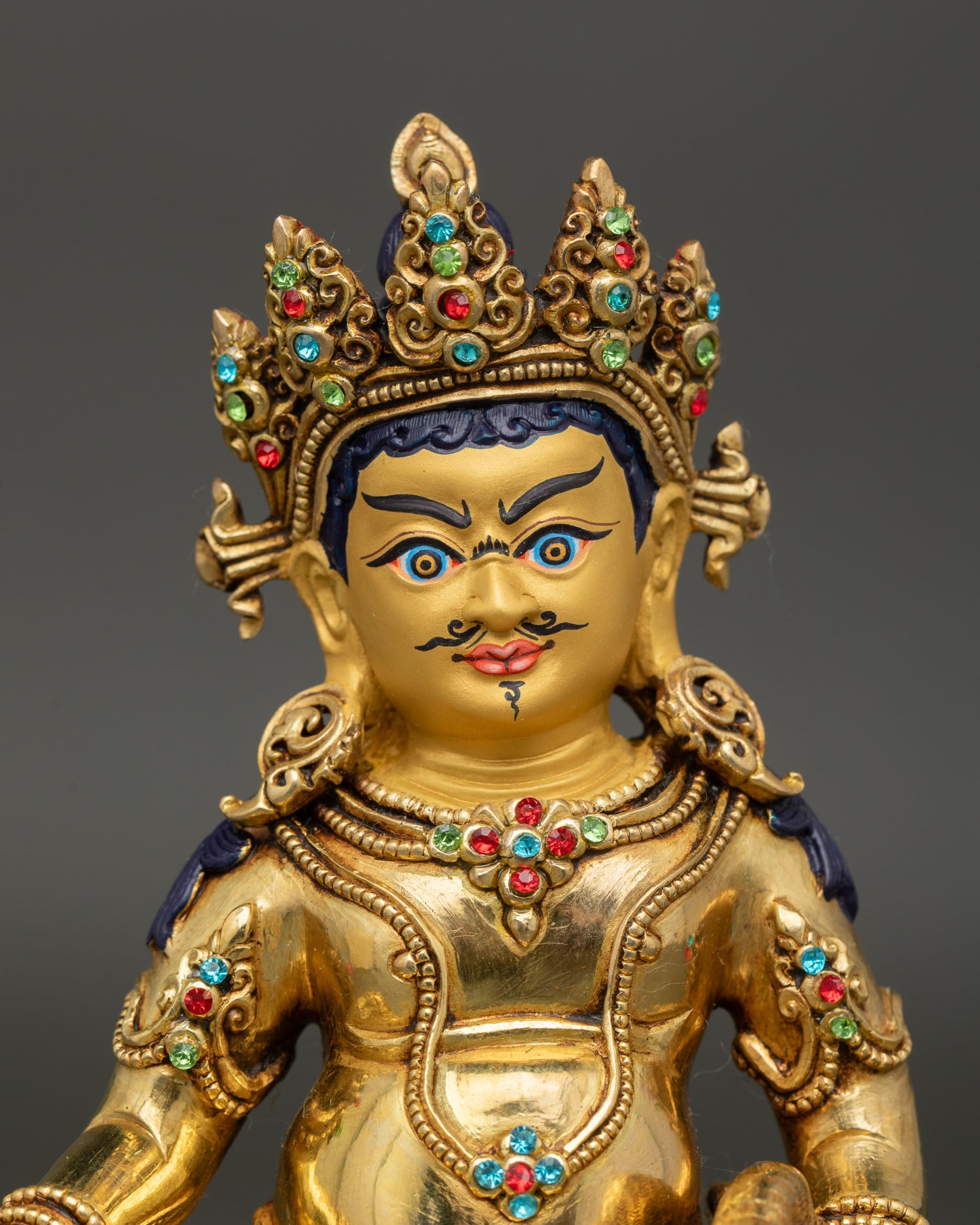 Close-up view of Dzambhala Buddha statue showing gold-painted face, intricate ornaments, and traditional details.