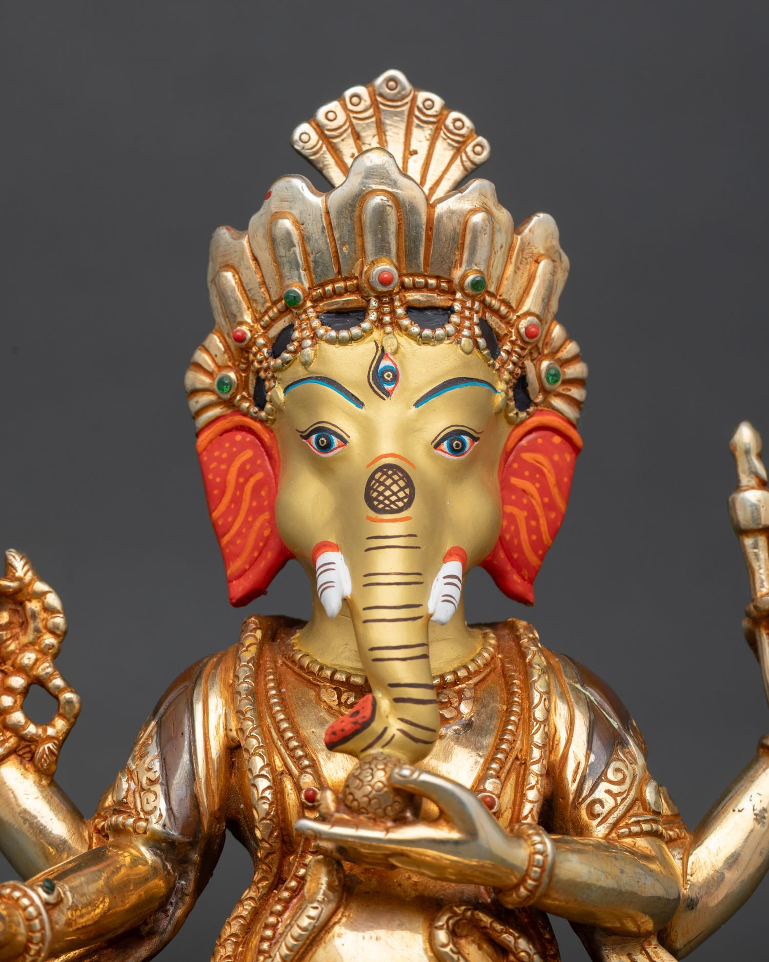 Close-up view of Ganesha statue with gold-painted face, intricate crown, and semi-precious stone detailing