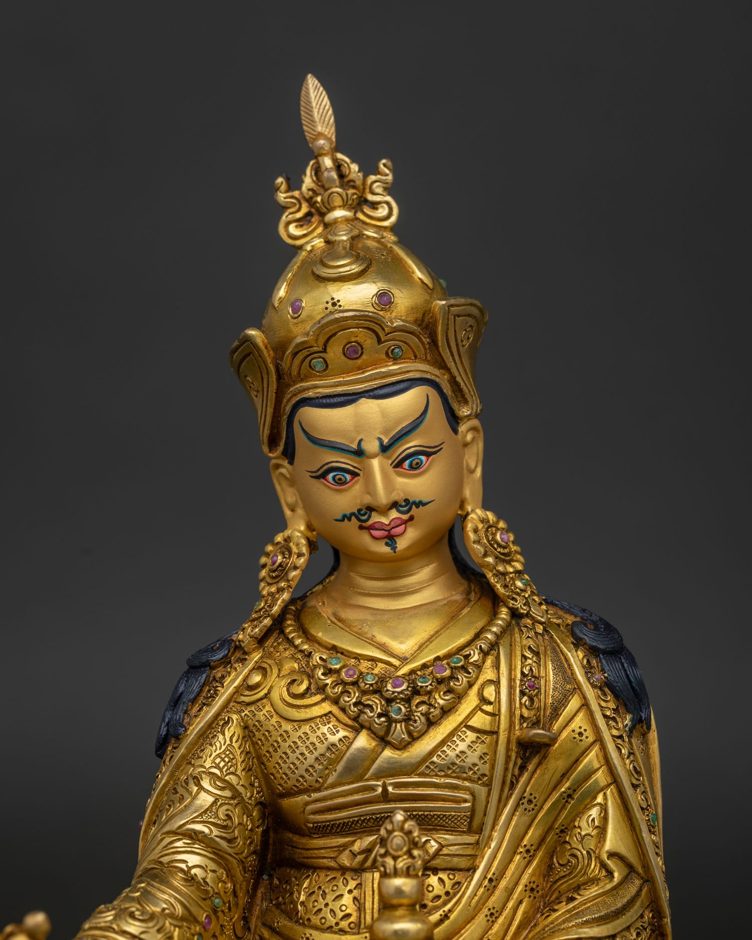 Close up view of Guru Rinpoche face with gold painted details and semi precious stone inlays