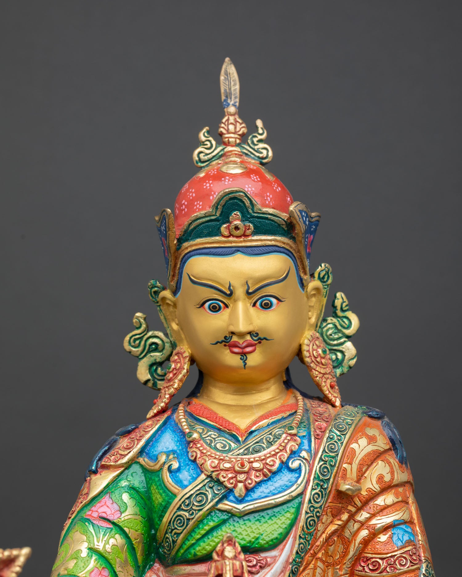 Close up view of Guru Rinpoche statue showing serene expression kasaya robes floral motifs and a gold-painted face detailing