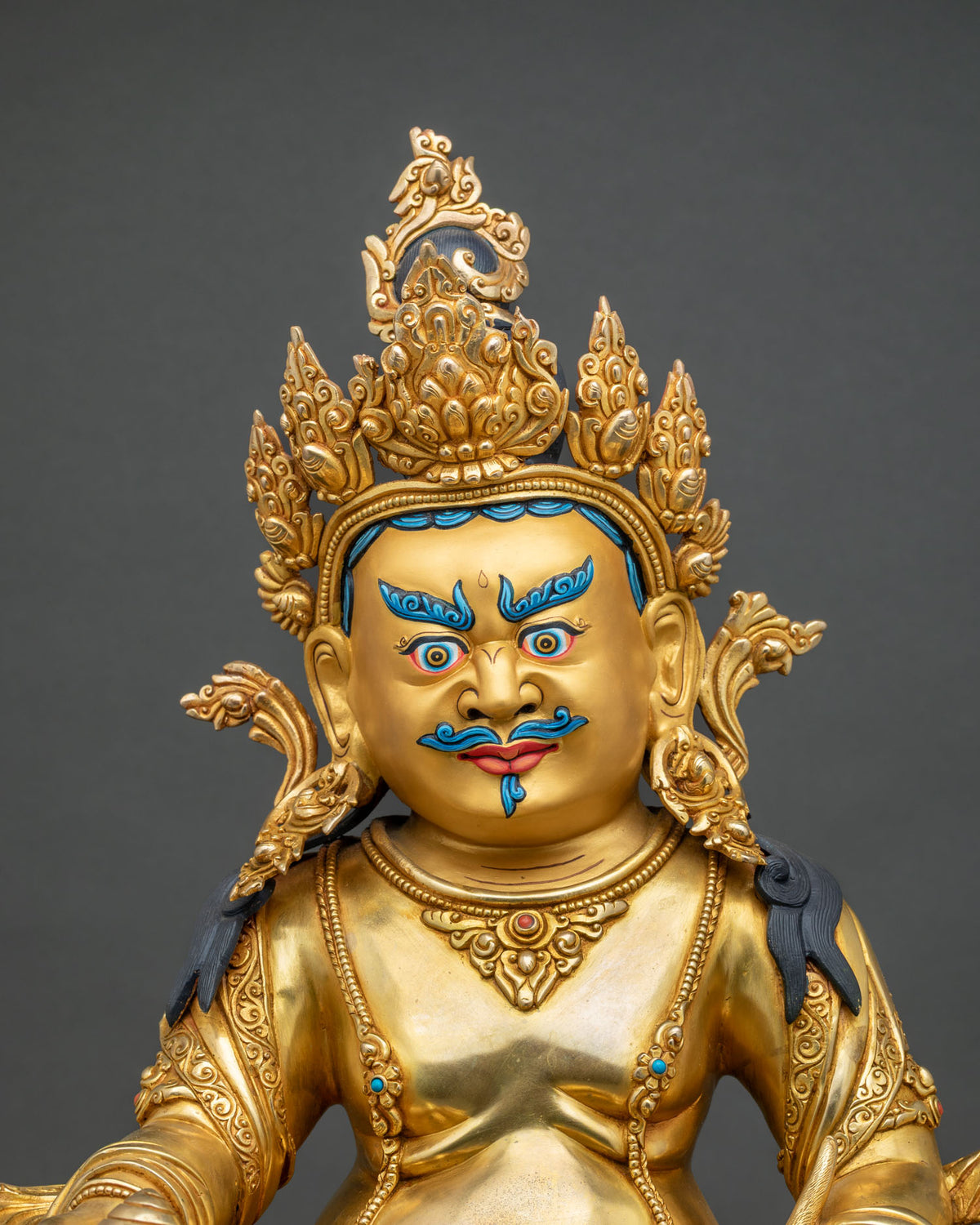 Close up view of hand carved gold gilded Yellow Dzambhala statue holding a jewel-spitting mongoose.