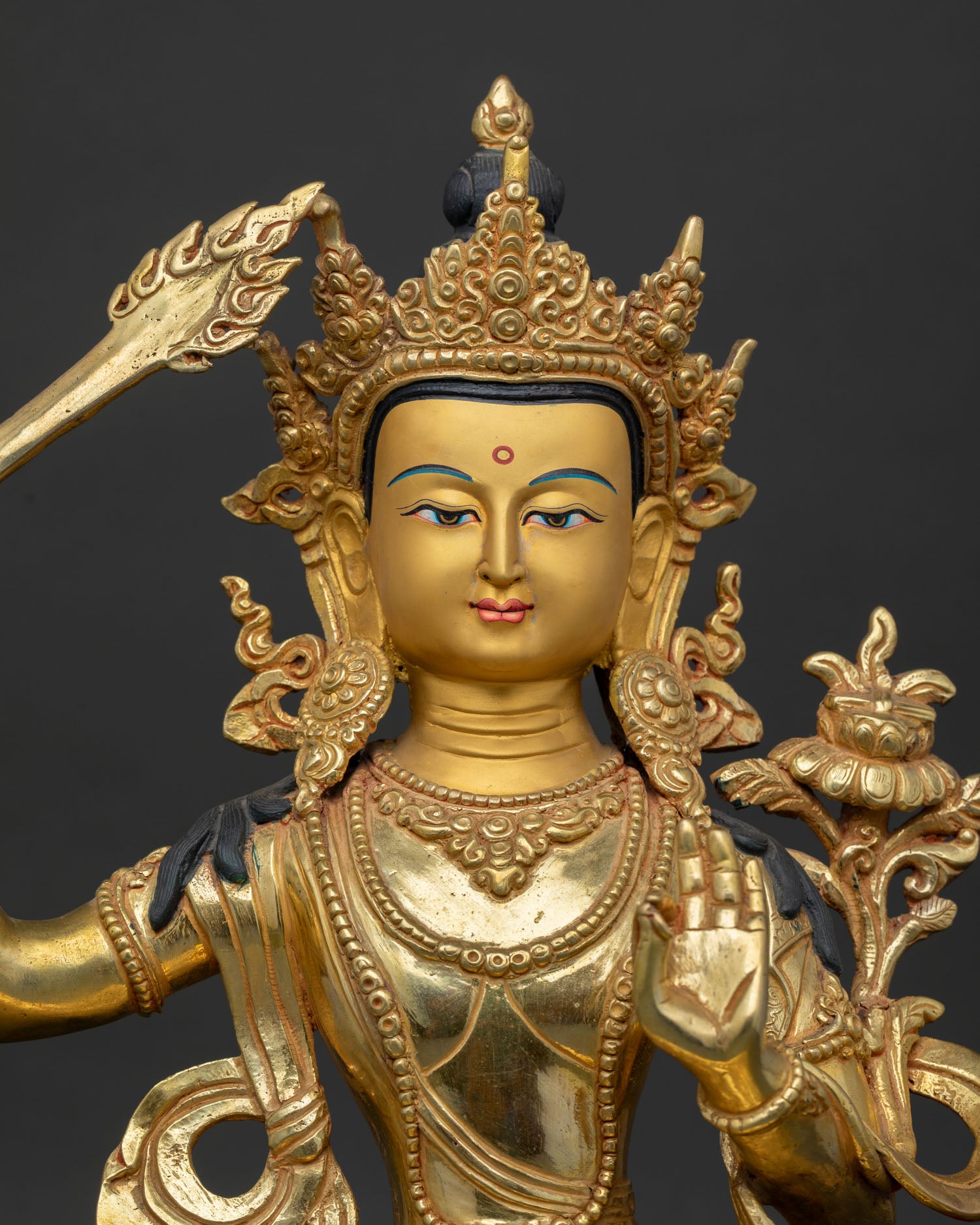 Close up view of Manjushri Statue with gold painted face and intricately carved robes.
