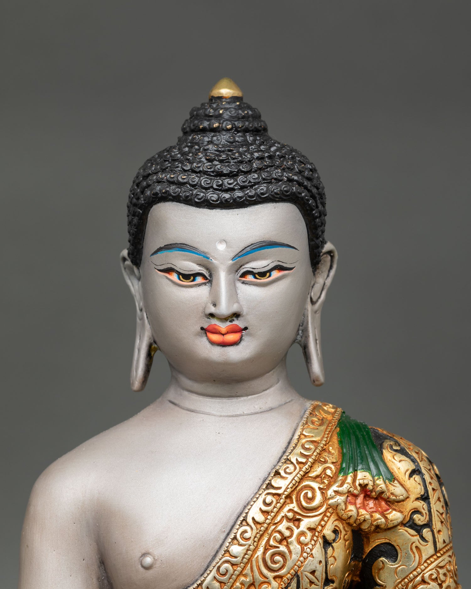 Close up view Shakyamuni Buddha statue serene face light grey body, gold accented robe Himalayan craftsmanship