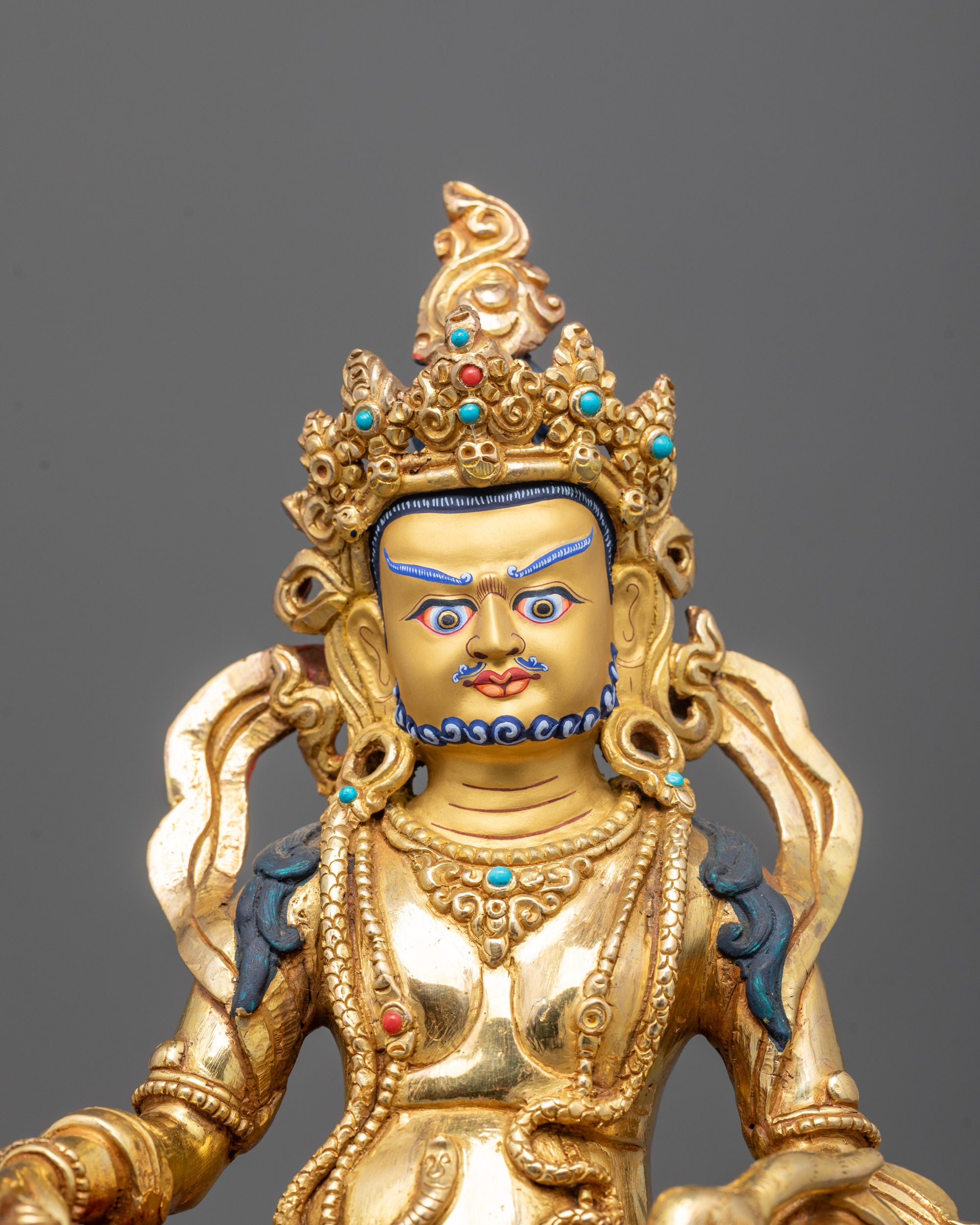 close-up Dzambhala face and mongoose with semi-precious stones and fire-gilded body details