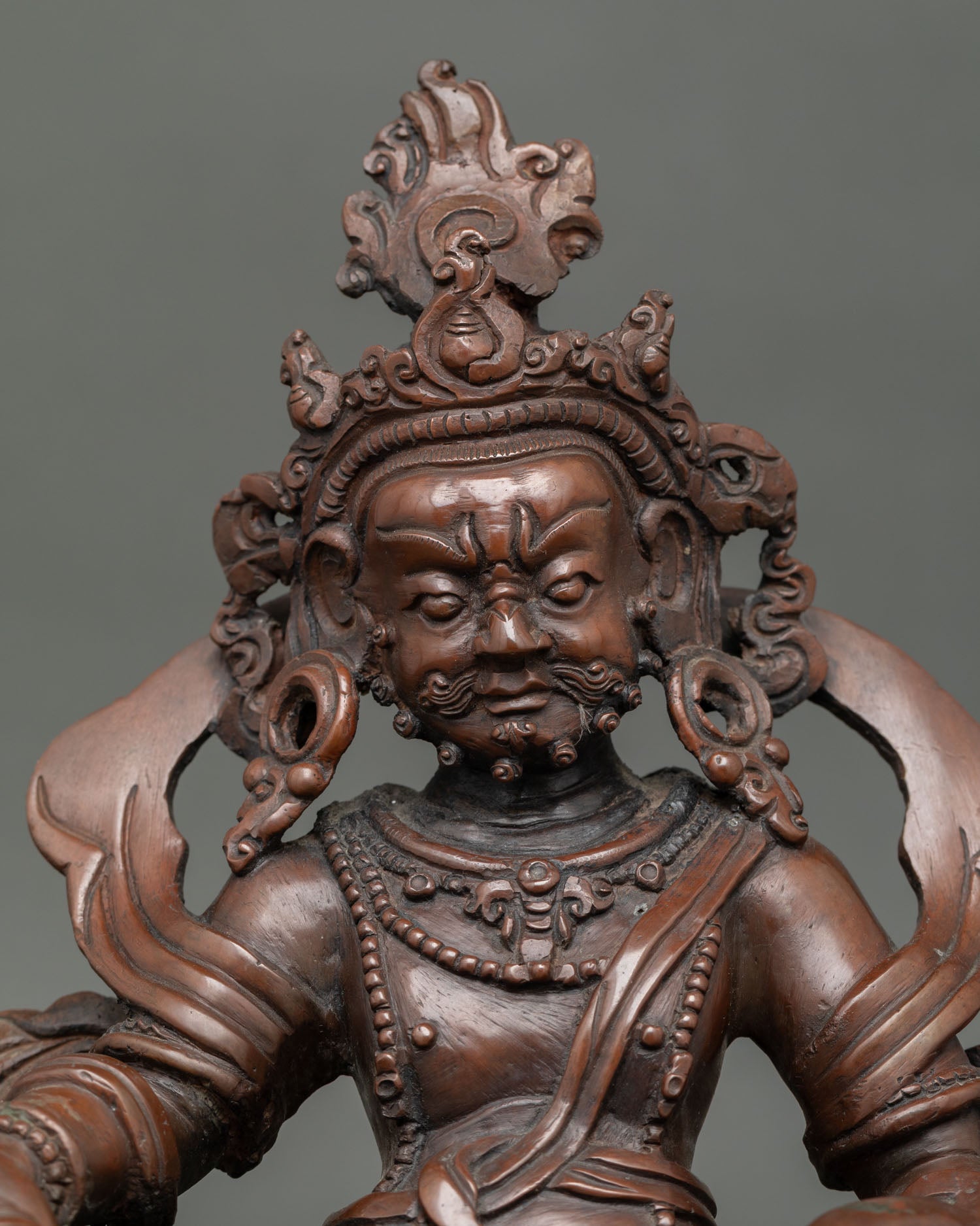 Close view of Dzambhala statue showing detailed oxidized copper craftsmanship and traditional Himalayan artistry.