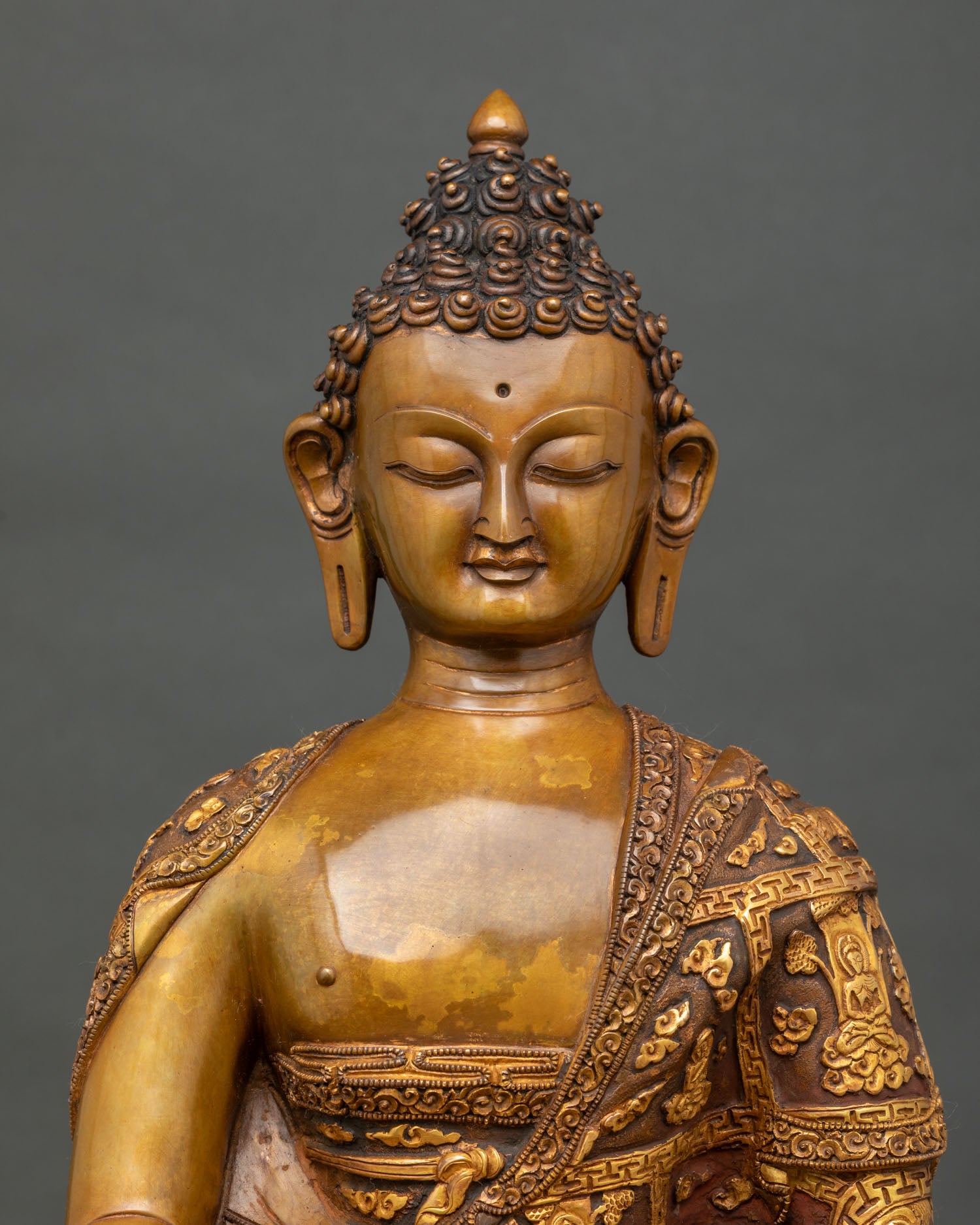 Close view of Shakyamuni Buddha statue with brown oxidized copper finish and intricately gilded monastic robe