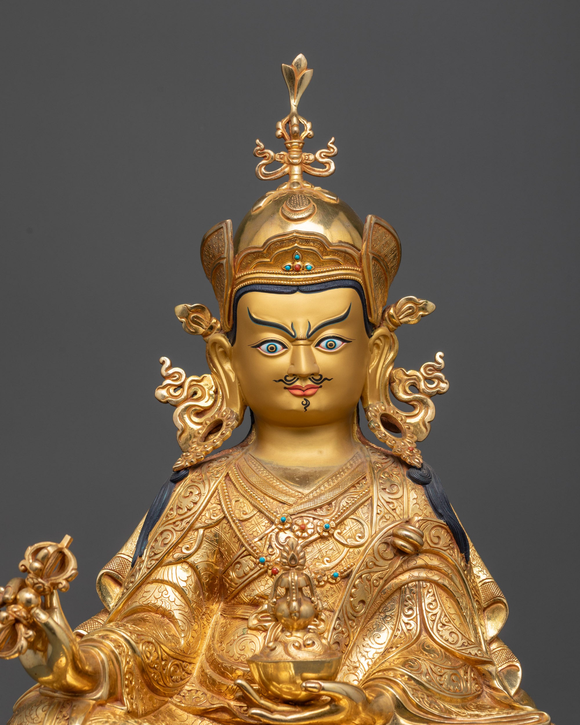 close up Guru Rinpoche statue holding skull cup, vajra and trident with kasaya robe