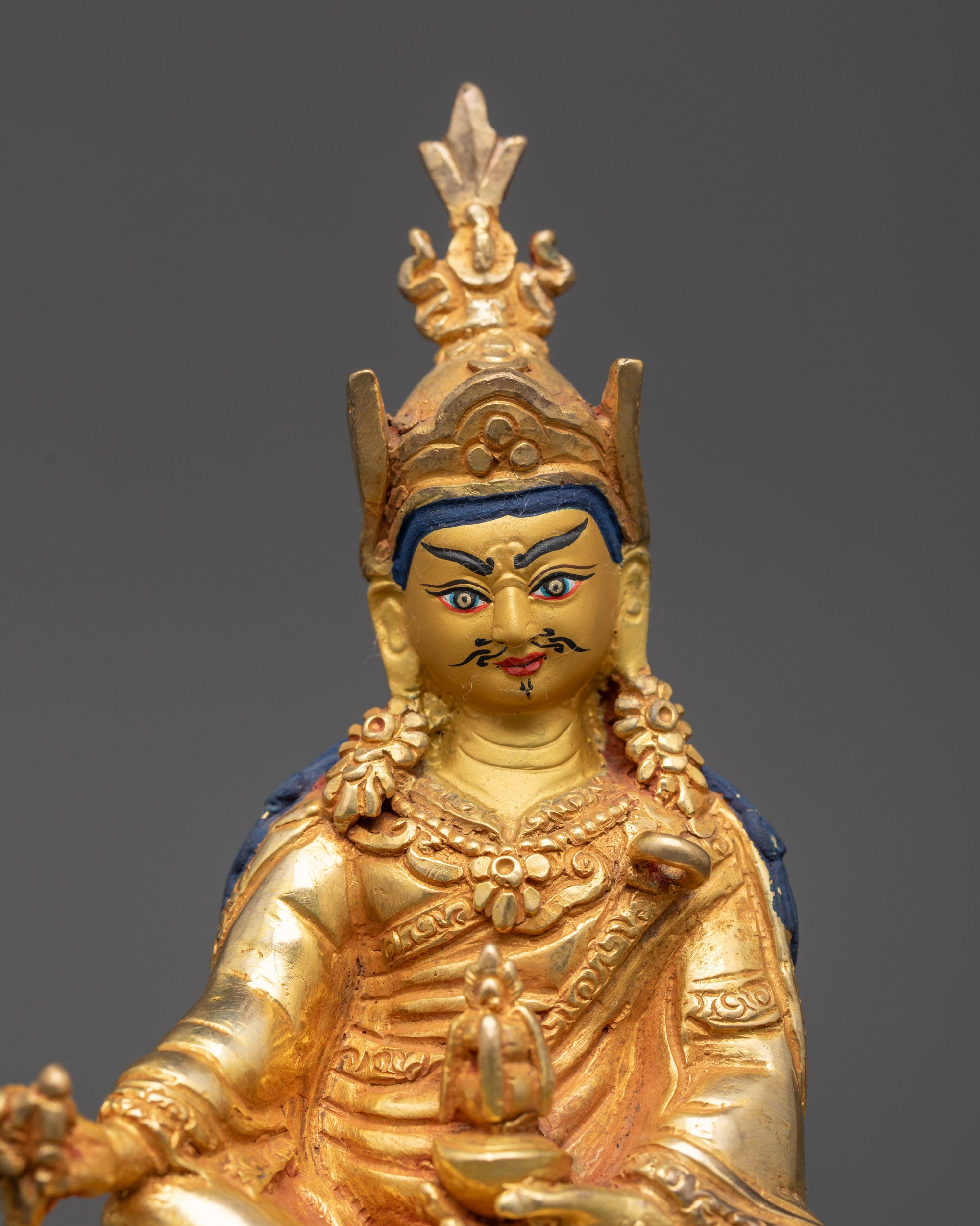 close up Guru Rinpoche statue showing lotus hat, robes, and ornate Himalayan ornaments