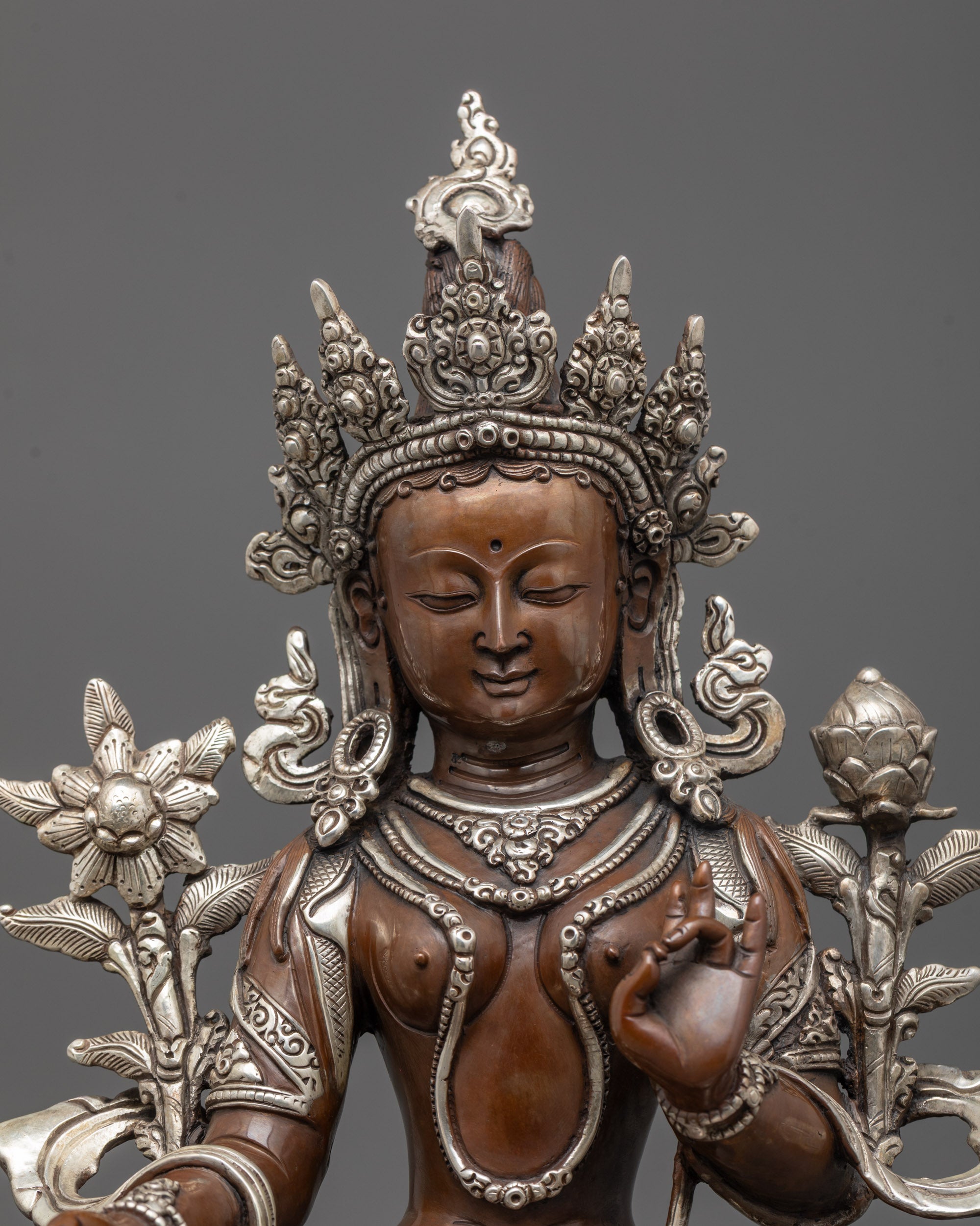 close up of green tara's silver-plated face, crown, and utpala flower symbolizing purity