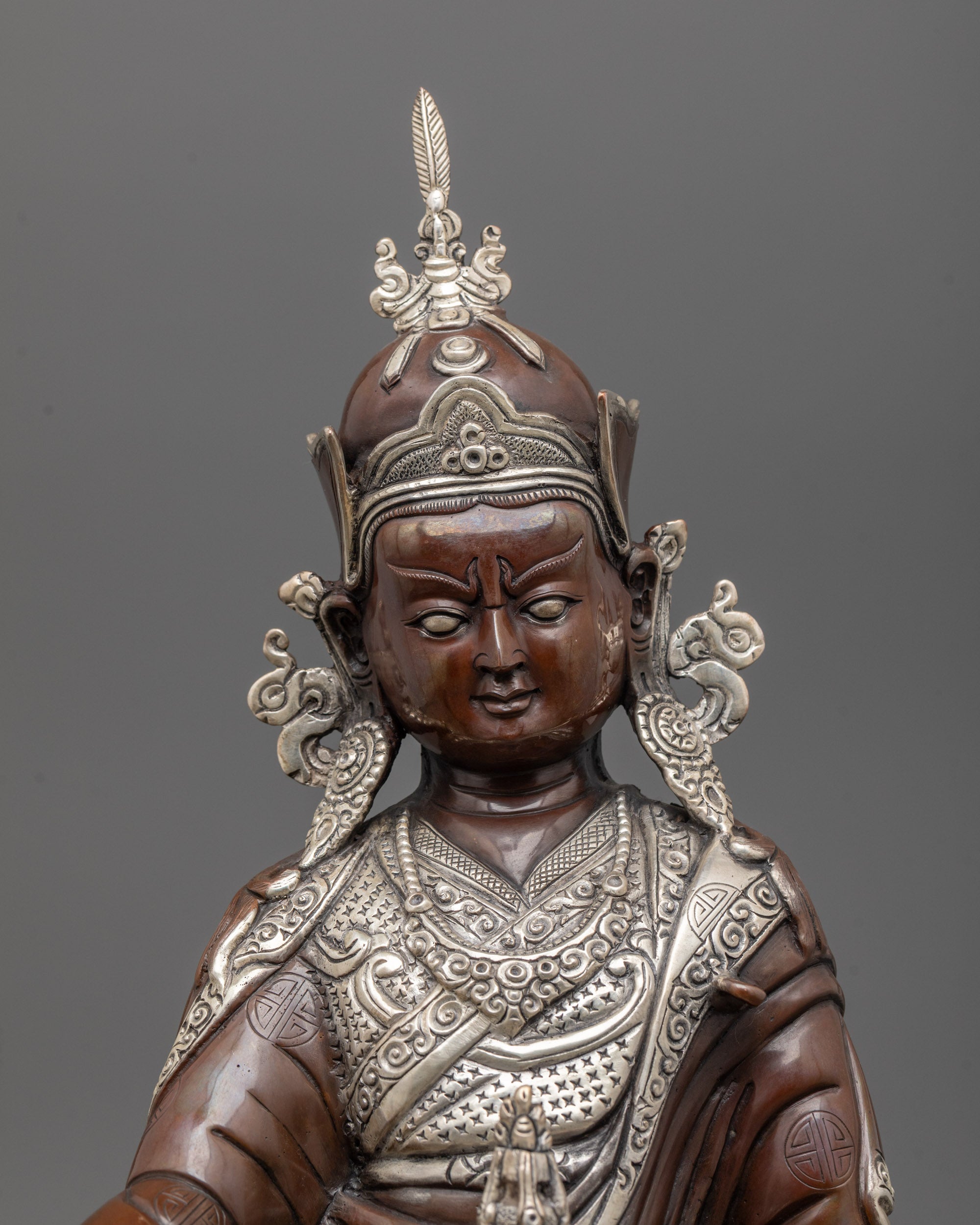 close up of guru rinpoche face with silver-plated lotus hat and serene expression