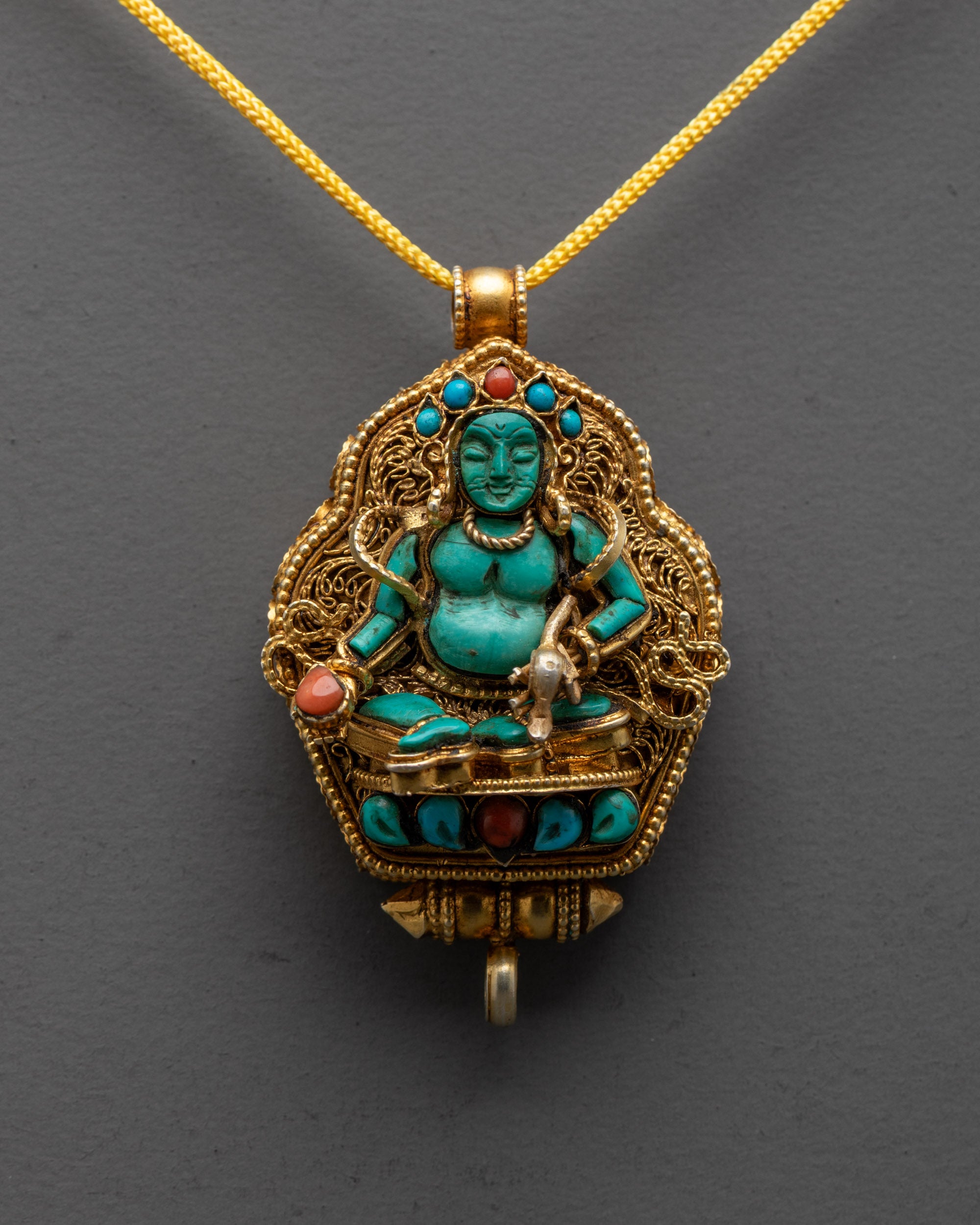 close up of turquoise Dzambhala figure holding jeweled spitting mongoose on gold pendant