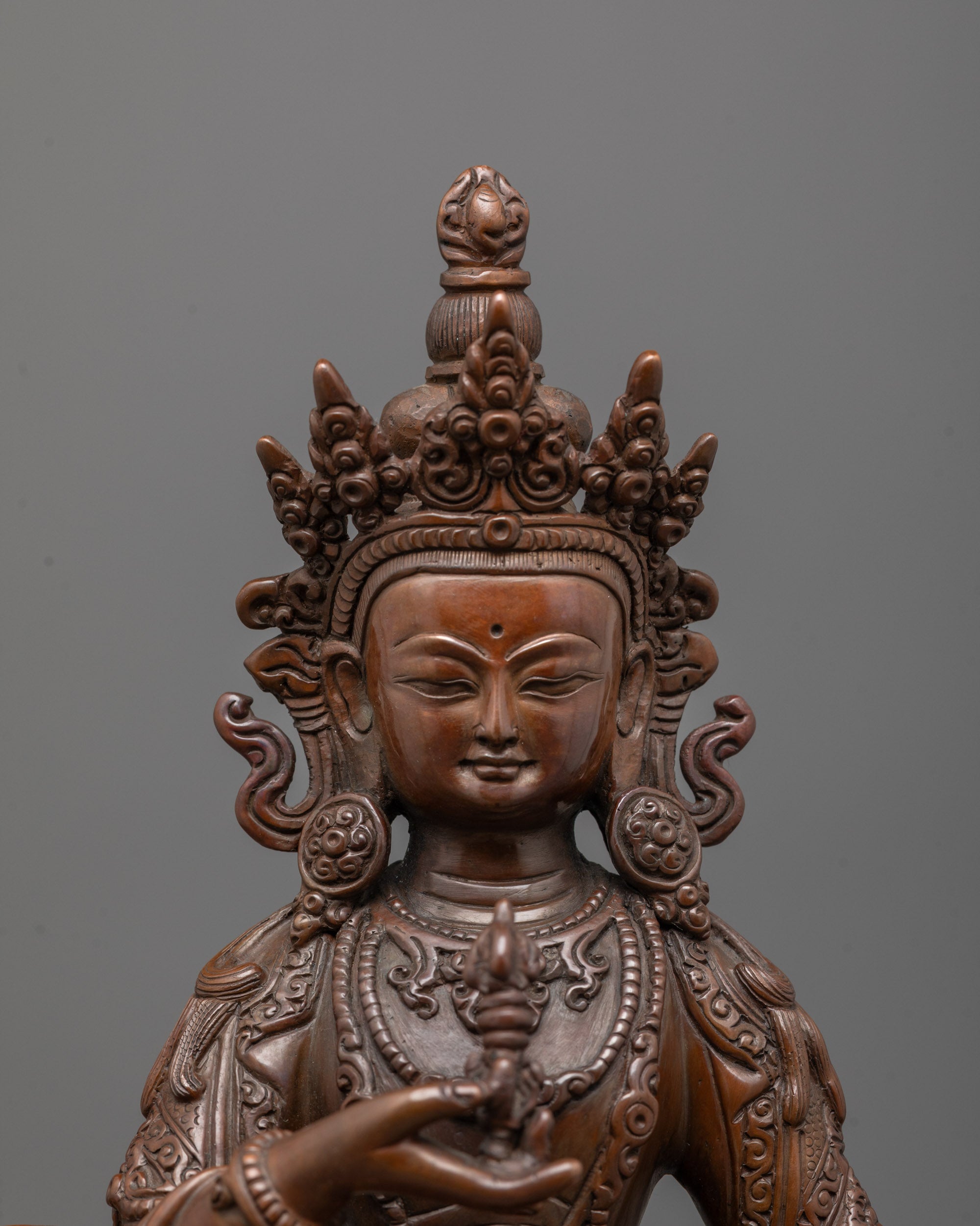 close up of vajrasattva statue showing detailed crown jewelry and serene oxidized copper face